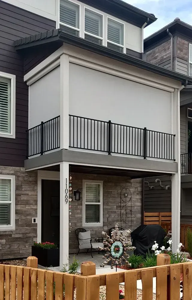 Two-story house with a porch. Porch has a retractable shade, black railing, and a wooden fence.