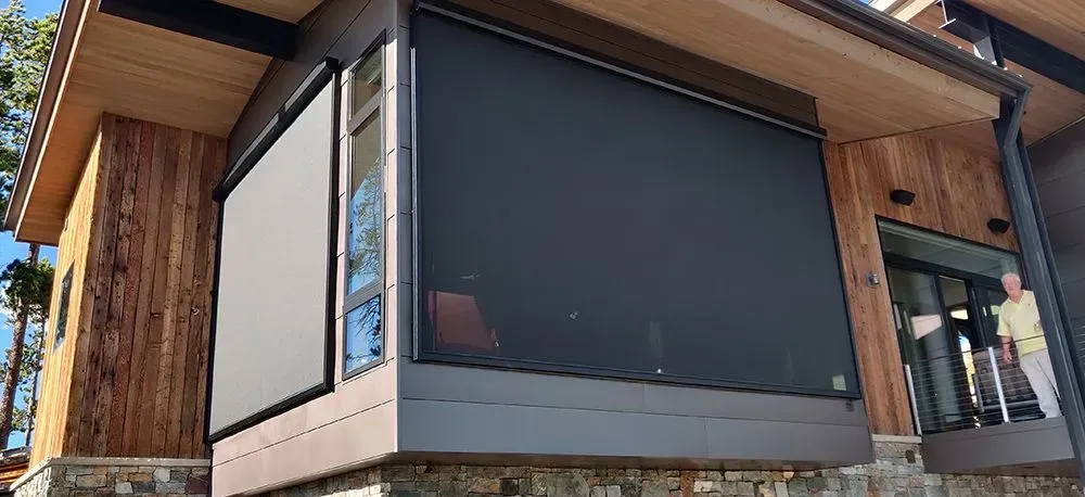 Exterior of a modern home with retractable black shades over windows, cedar siding, and stone foundation.