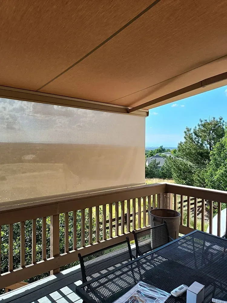 A deck with a retractable awning. A table and chairs sit on the deck, and trees and sky are visible.