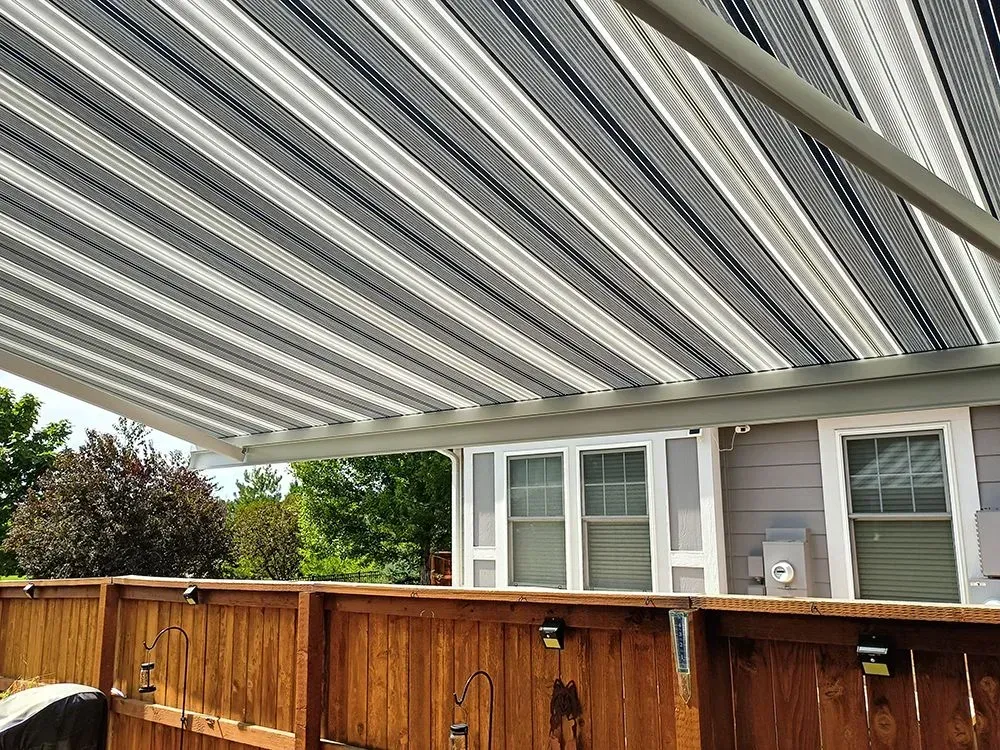 Striped awning over a wooden fence and house, providing shade.
