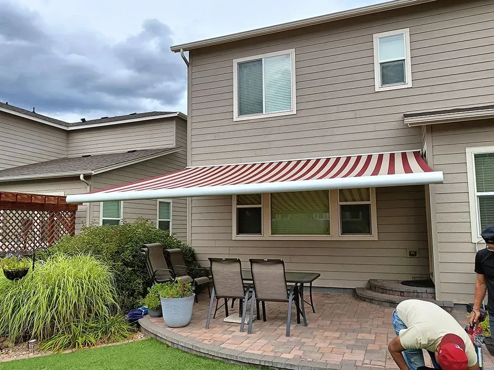 A house with a red and white striped awning over a patio with a table and chairs; a person is working.