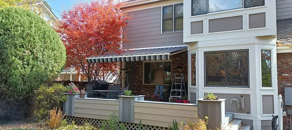 A house with a deck and an awning in the autumn. A person is on a ladder.