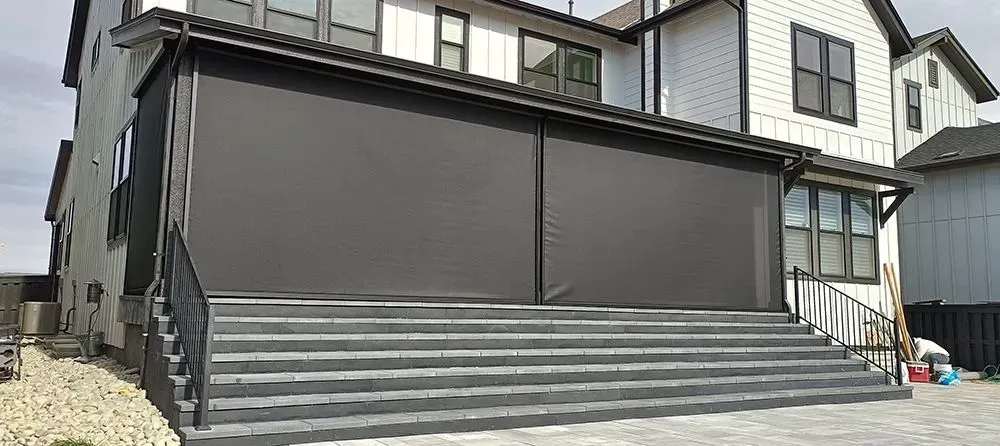 Gray porch with dark curtains, steps, and black railing on a modern house.