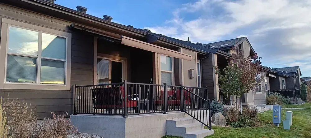 Row of townhouses with patios, dark roof, grey siding, and black railings. Blue sky overhead.