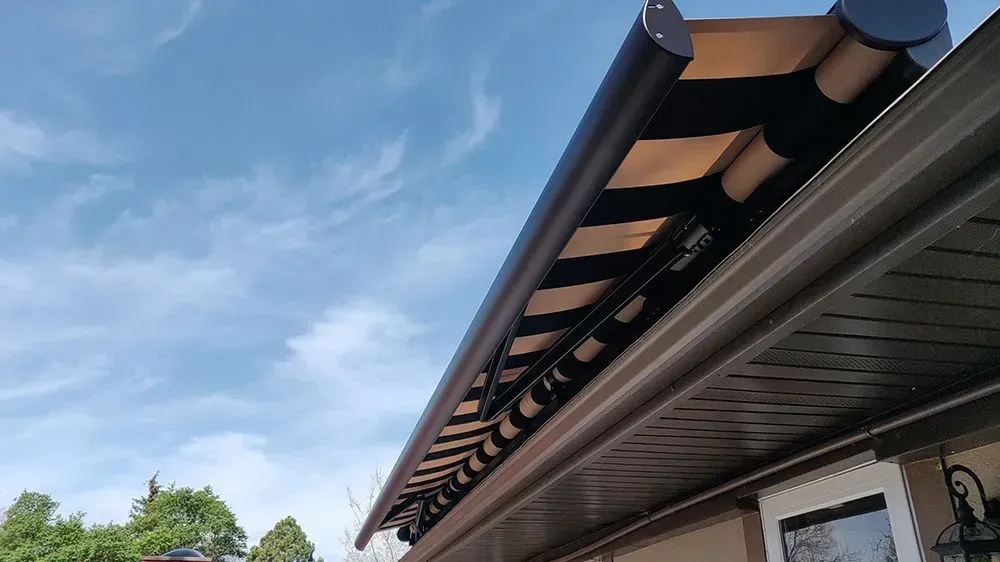 A brown and tan retractable awning installed on a house with a blue sky background.