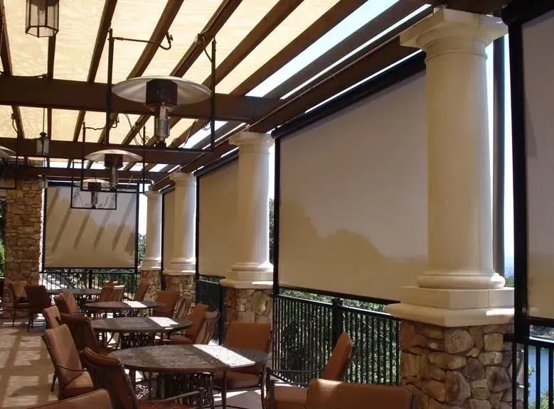 Outdoor dining area with retractable sun shades, beige awnings, and columns.