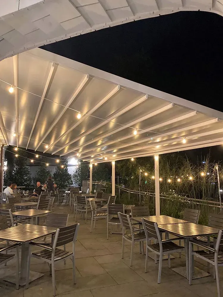 Outdoor restaurant patio at night, tables and chairs under a lit retractable awning.