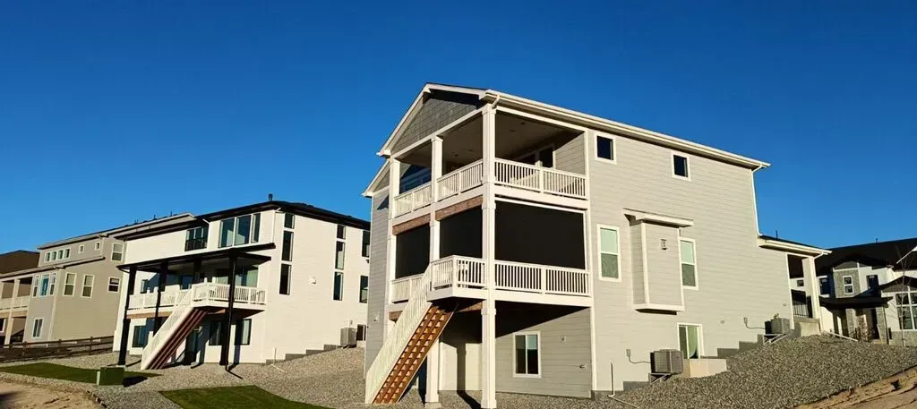 Multi-story houses with balconies under a blue sky, constructed on a rocky slope.
