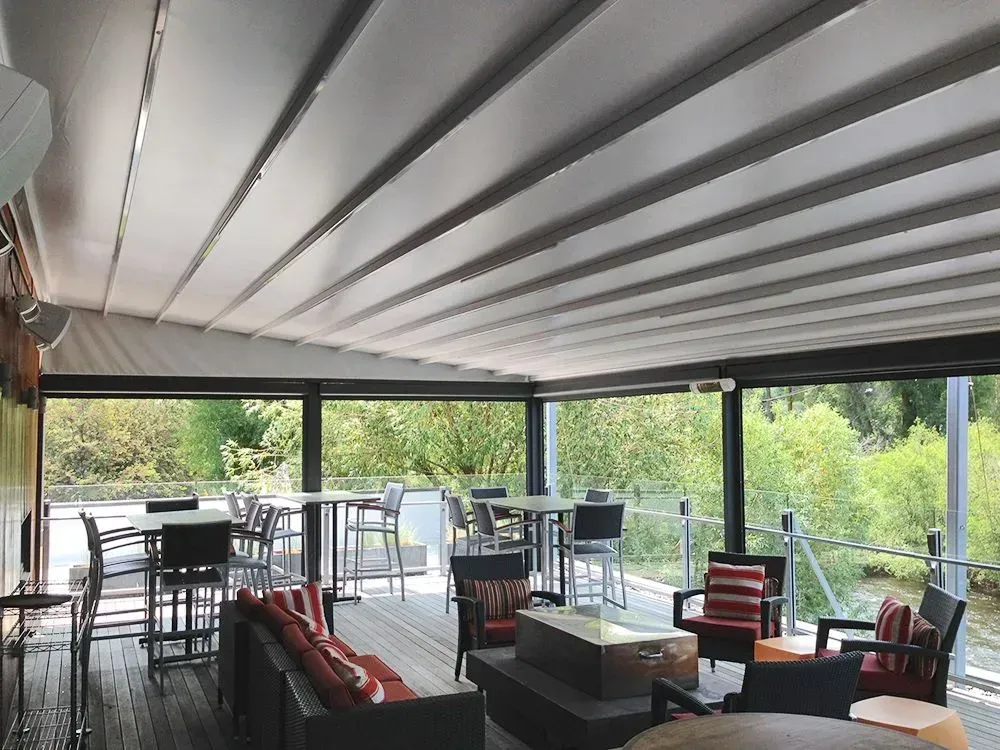 Outdoor patio with retractable roof, tables, chairs, and surrounding trees.