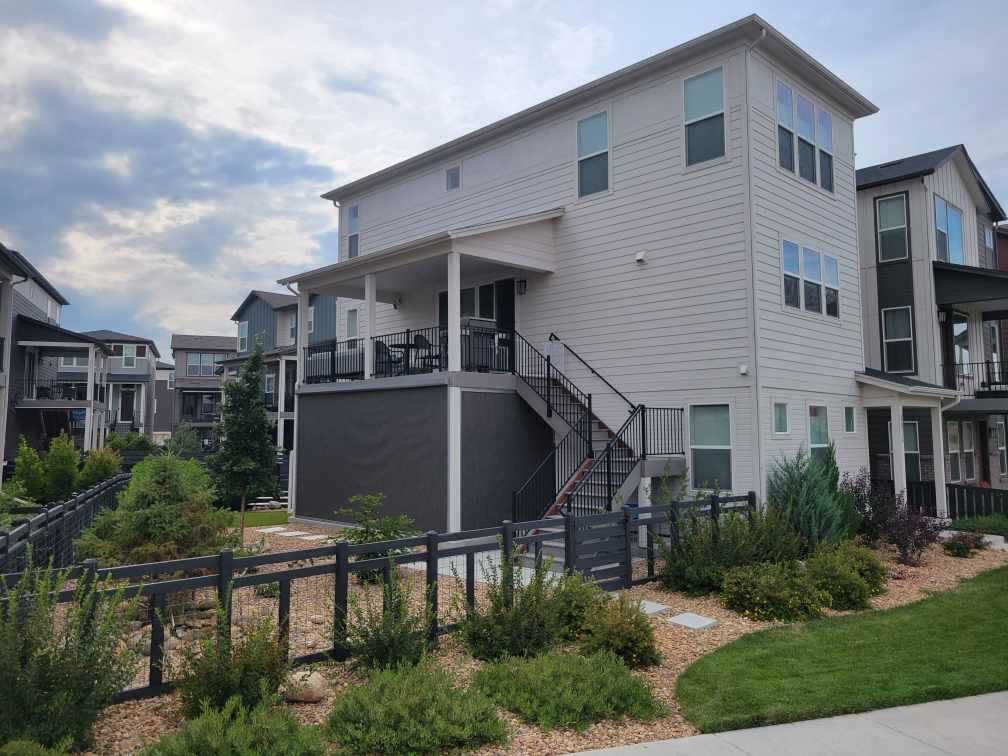 Back of a two-story modern house with a porch and stairs leading down to a fenced yard with landscaping.