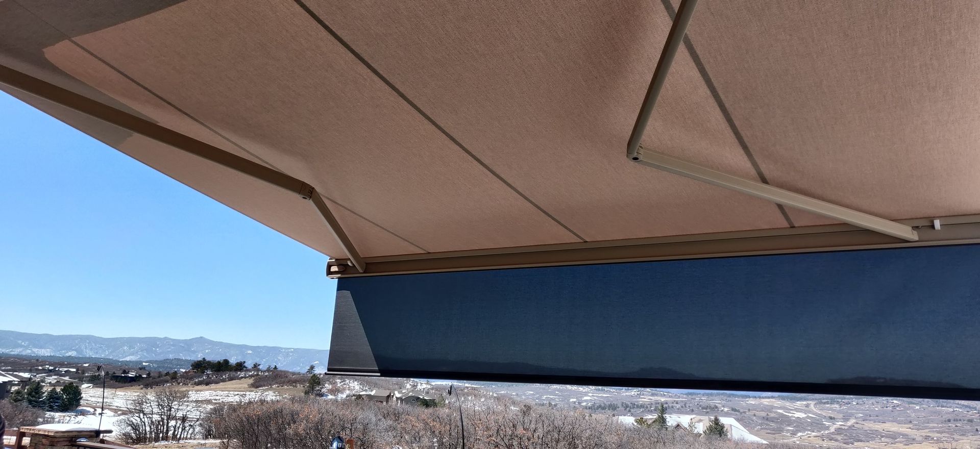 Beige awning over a blue wall and a distant landscape under a clear sky.