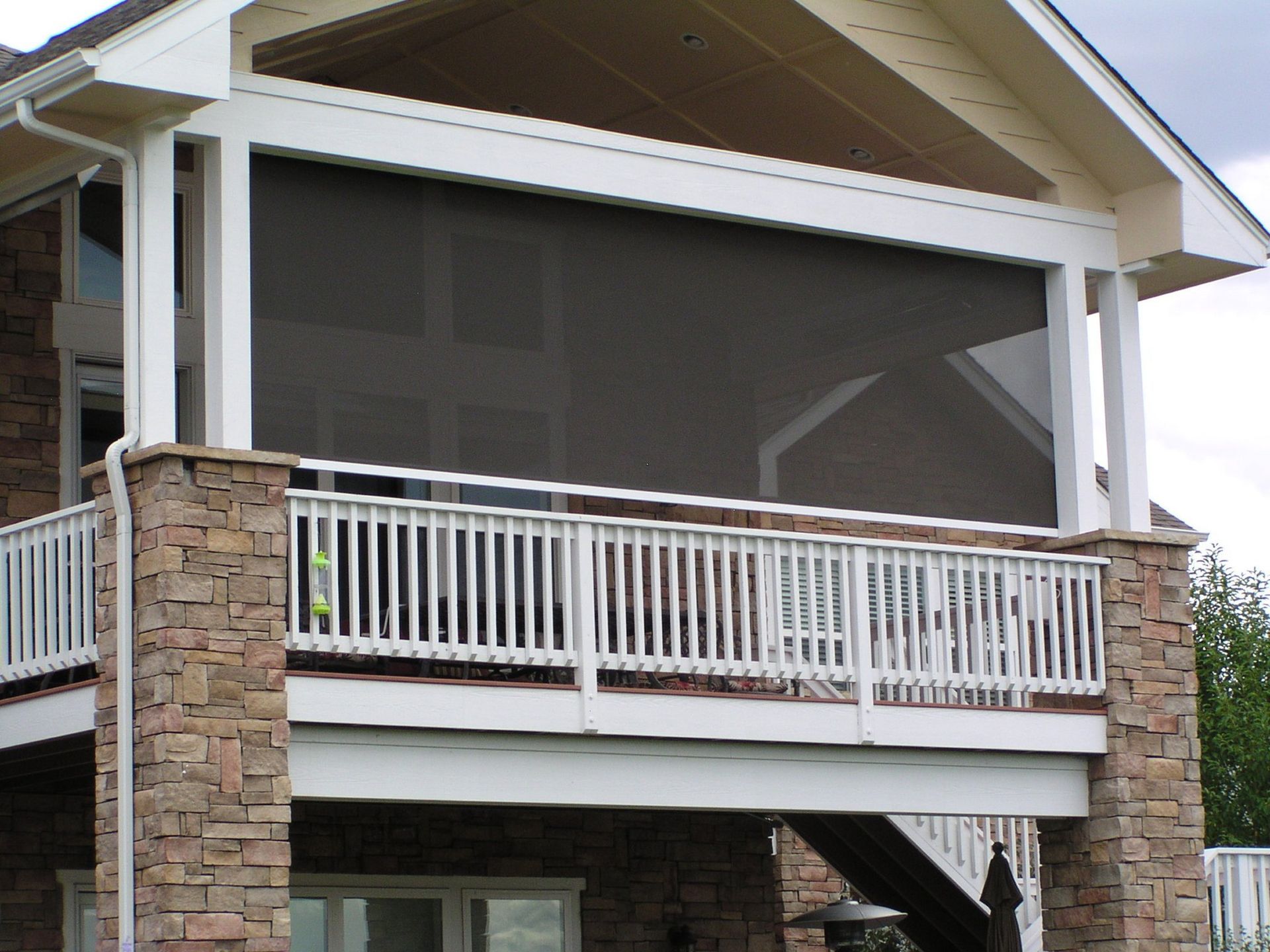 Screened-in porch with white trim, brown stone pillars, and dark mesh screens. A white railing is in front.