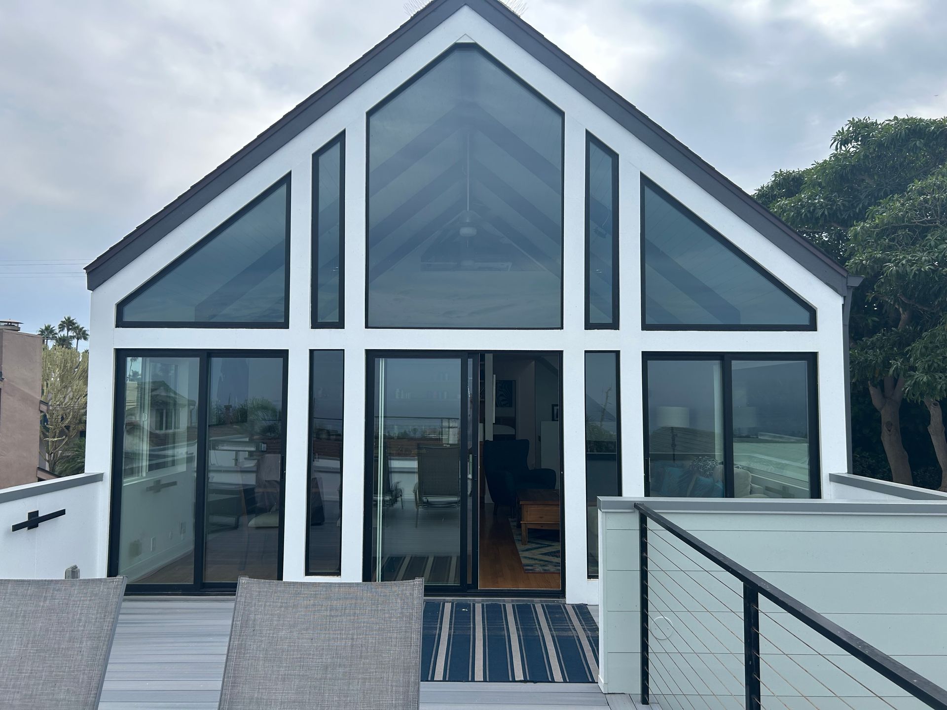 Modern white house with black trim, large glass windows, and a rooftop deck overlooking an outdoor space.