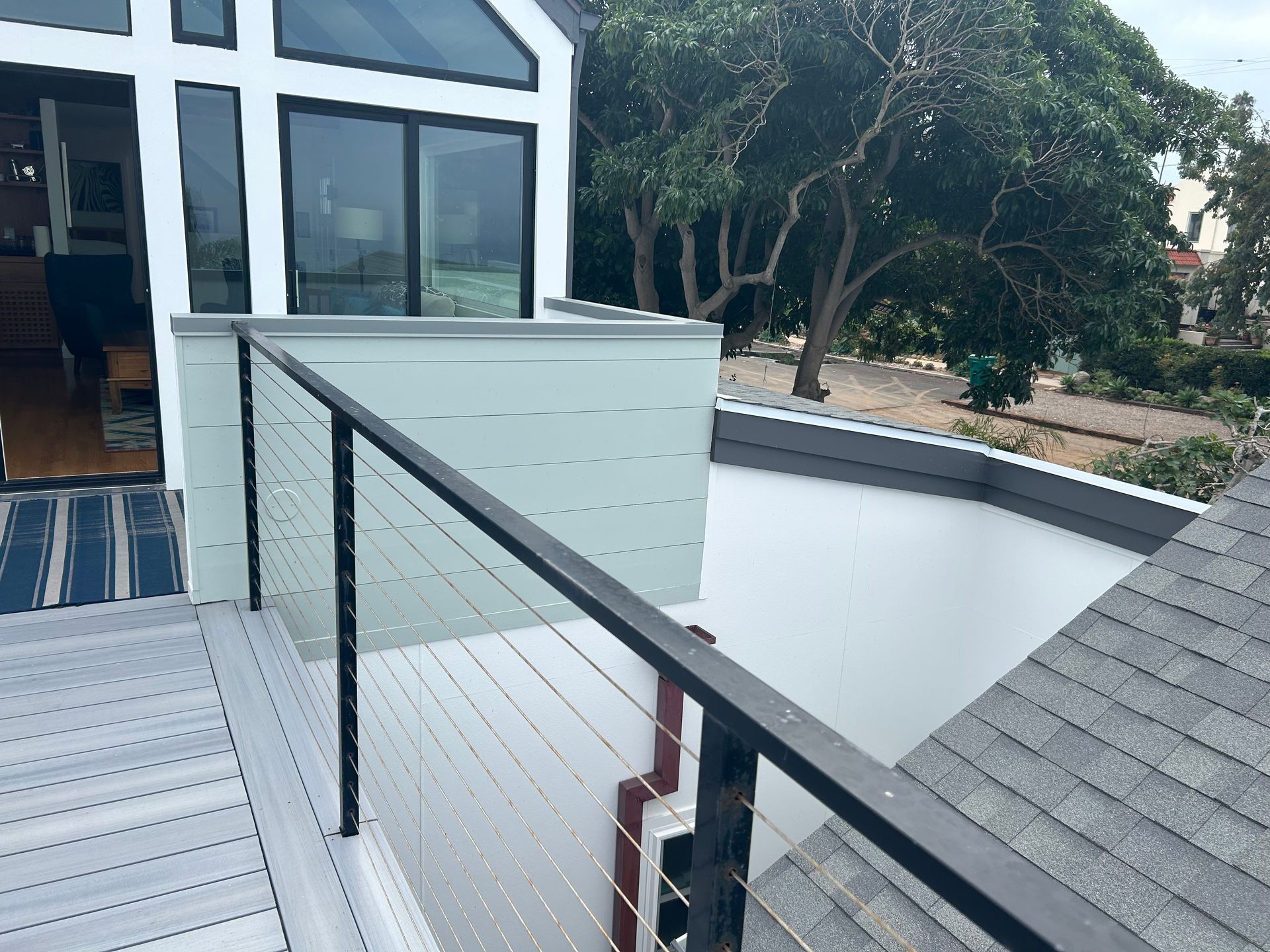 Modern house exterior with a balcony, metal railing, and view of trees.