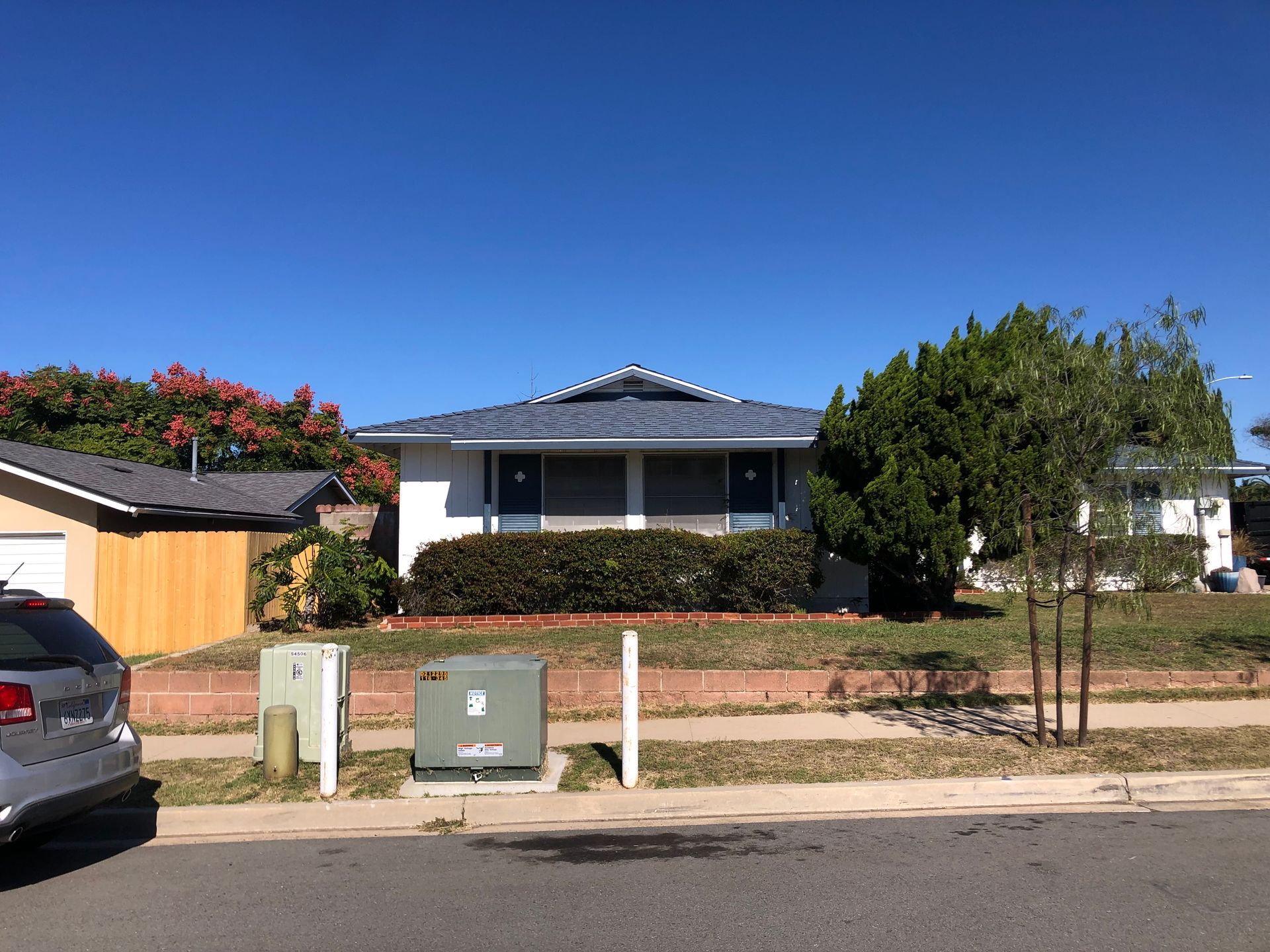 A white house with a blue roof, green bushes, and a blue sky.