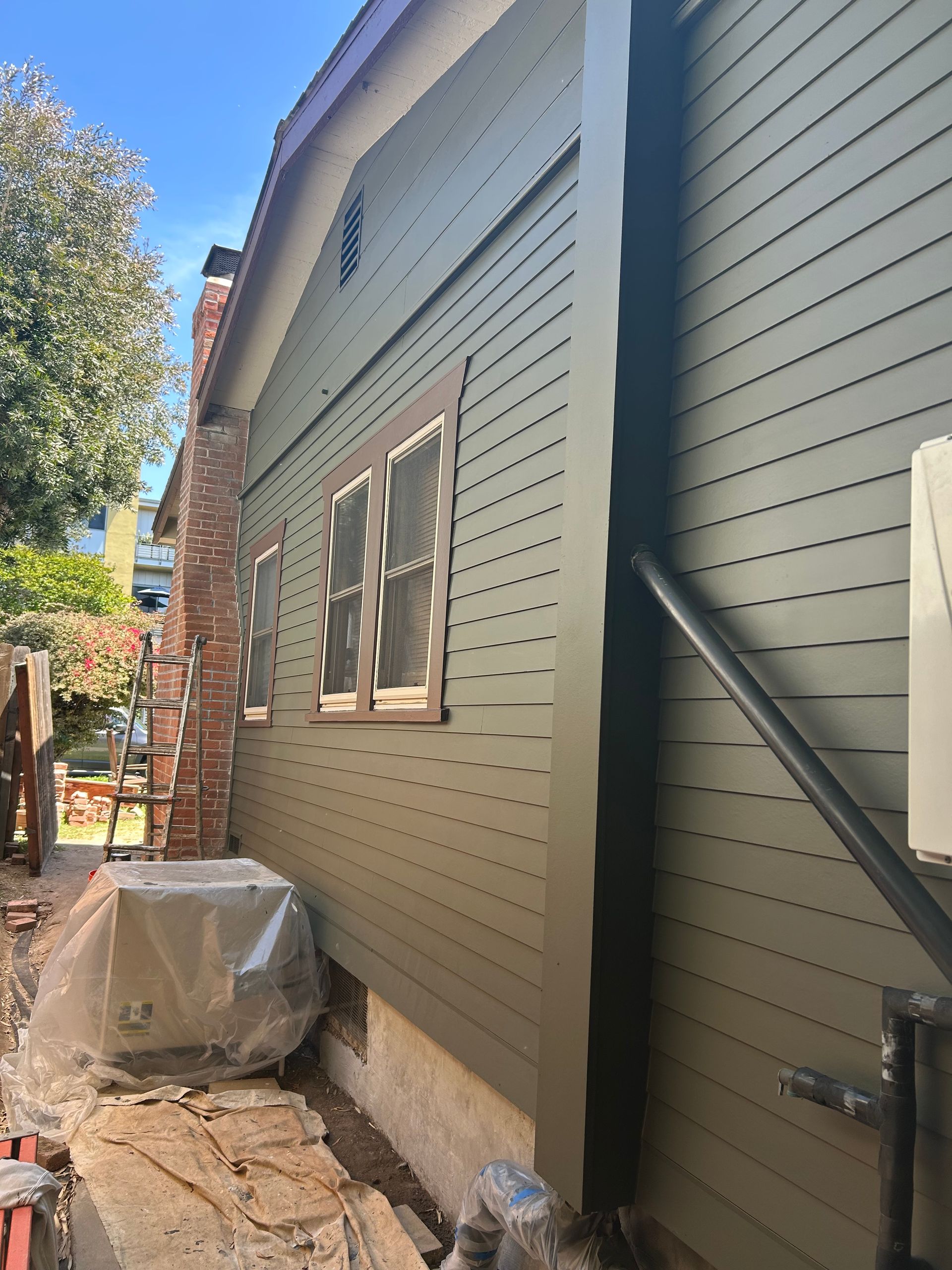 Side of a house with green siding, brown window frames, and a brick chimney.