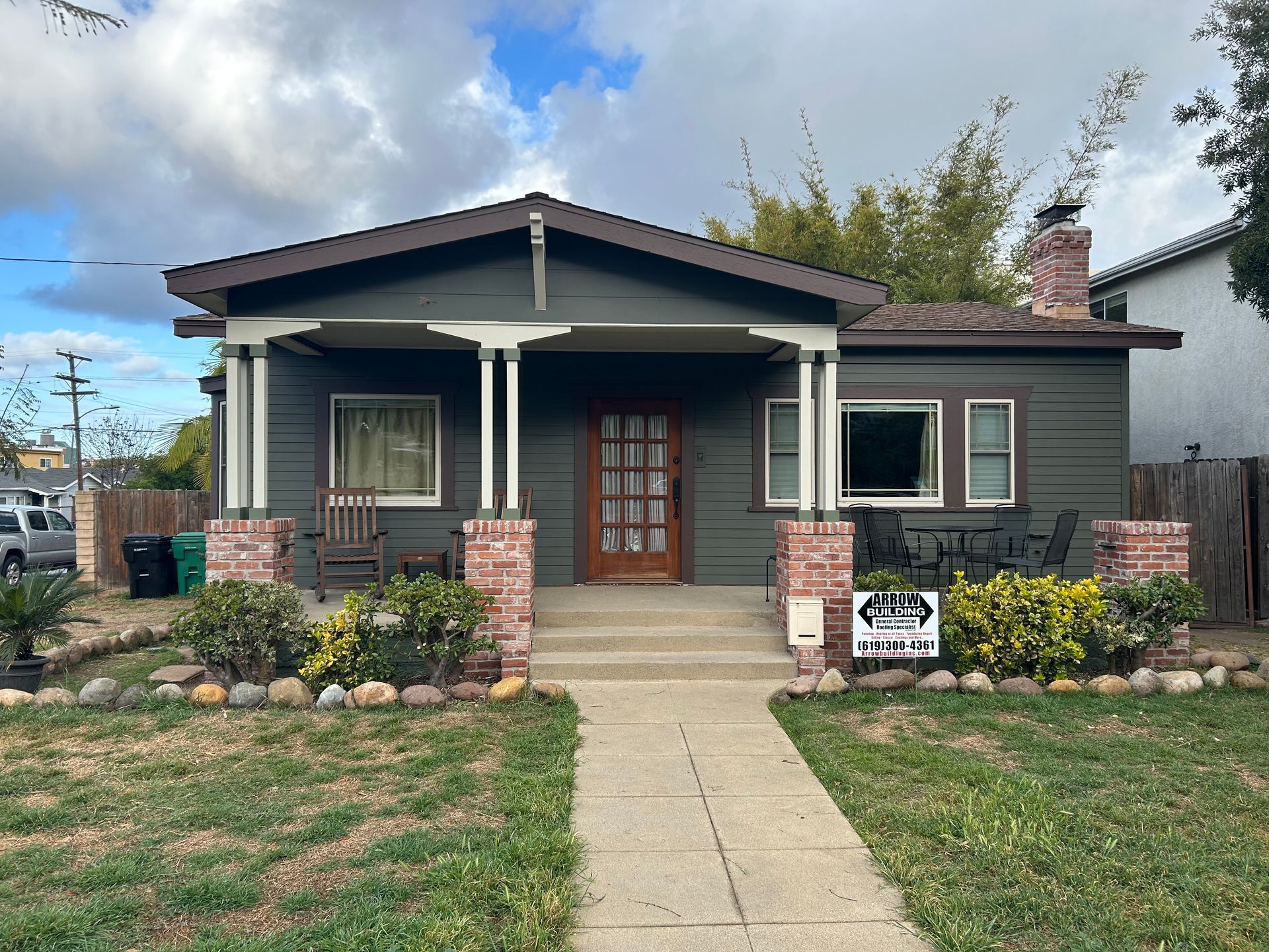 Green bungalow with brick accents, porch, and a walkway leading to the front door.
