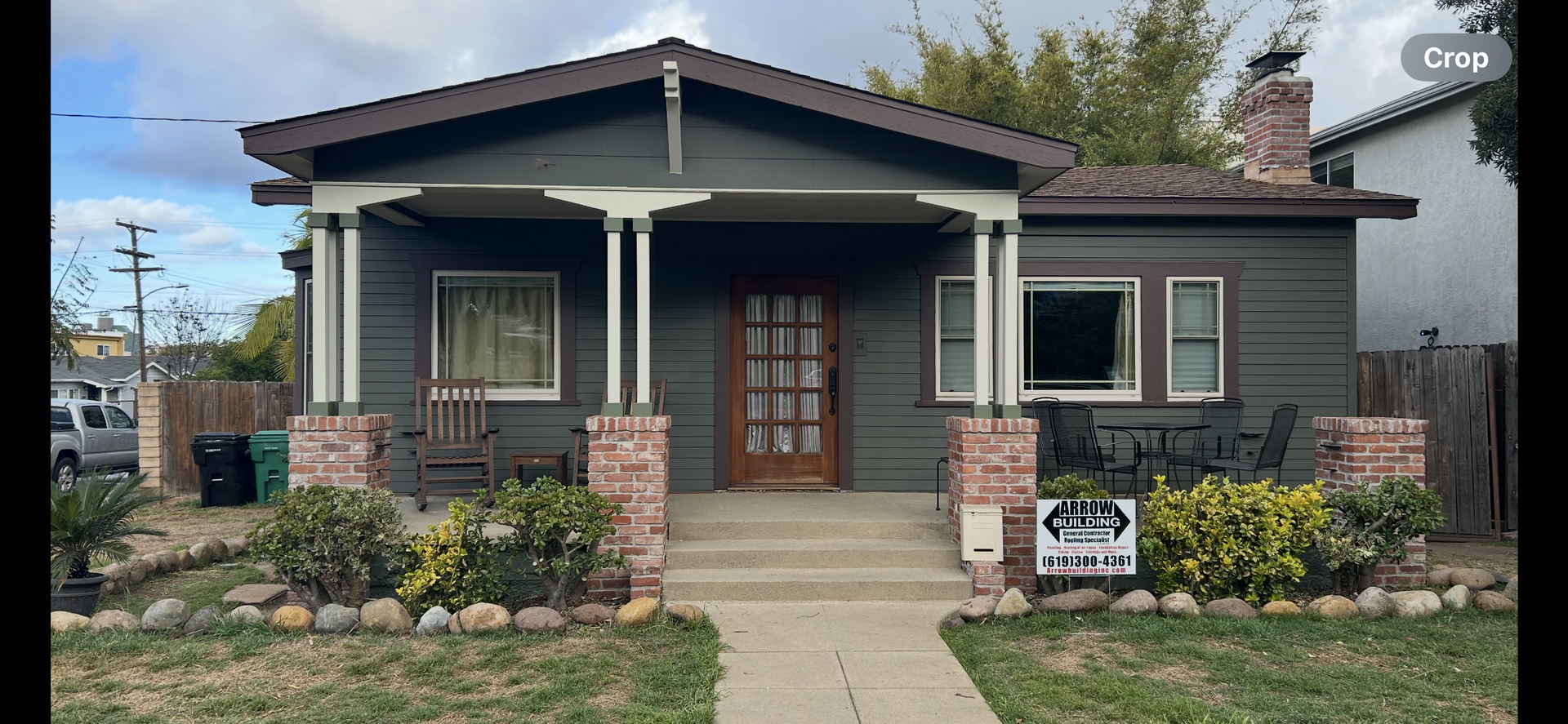 A green house with a porch and brick pillars. There is a sign that says