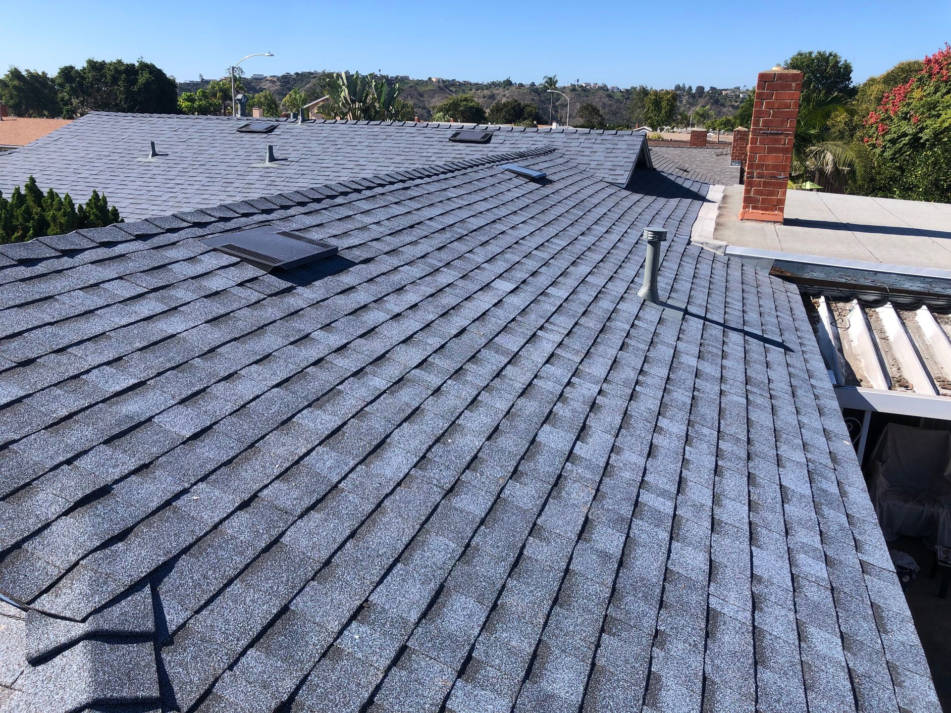 A close-up view of a gray asphalt shingle roof on a sunny day.