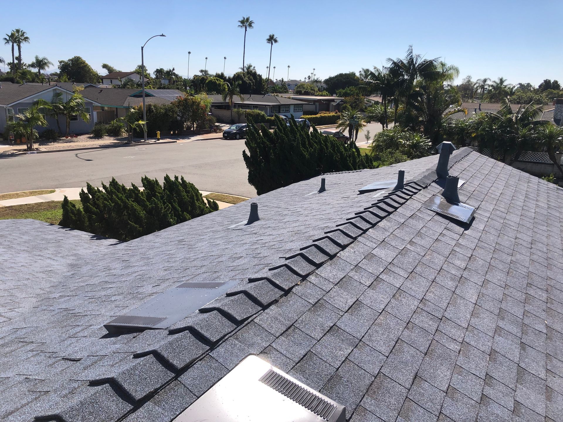View of asphalt shingle roof with vents and a street in the background on a sunny day.