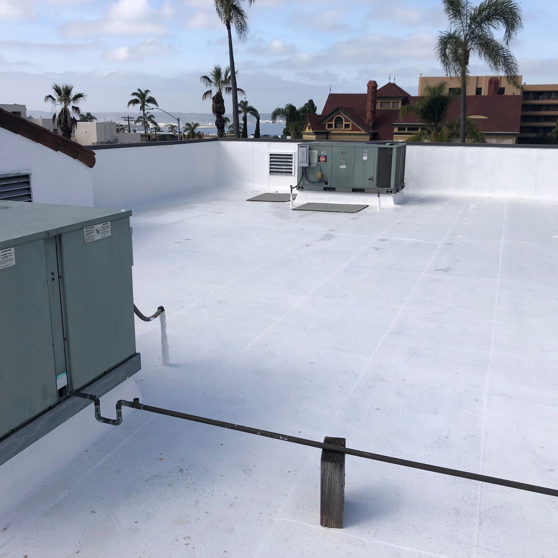 White commercial rooftop with HVAC units, ocean view, and palm trees.