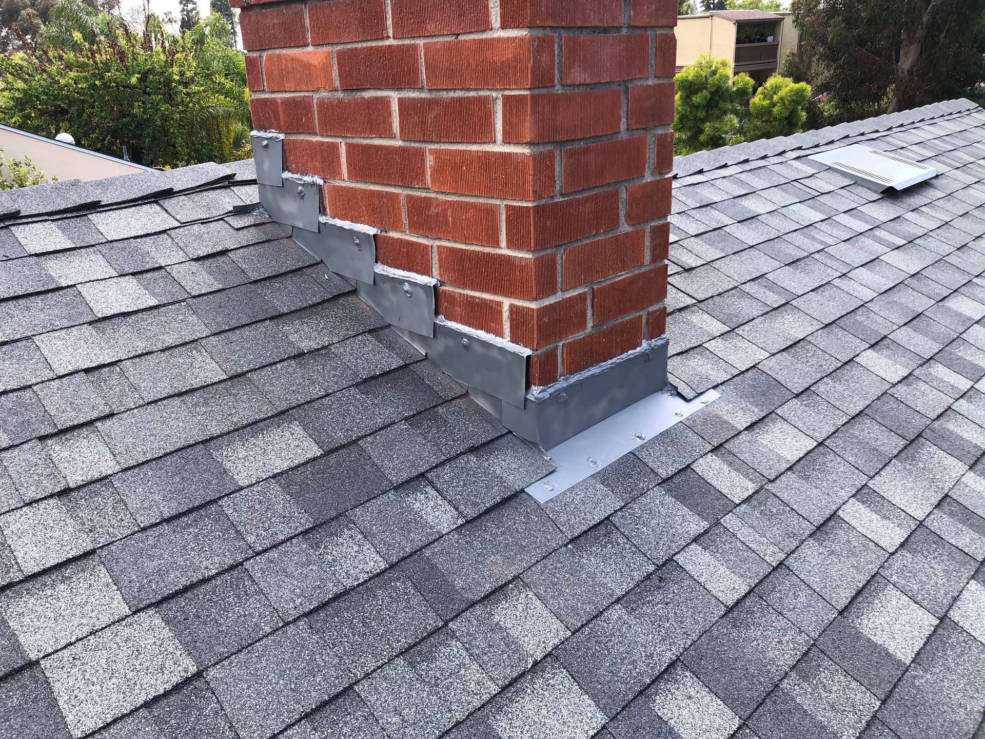 Chimney on a shingled roof with flashing; brick chimney, gray shingles.