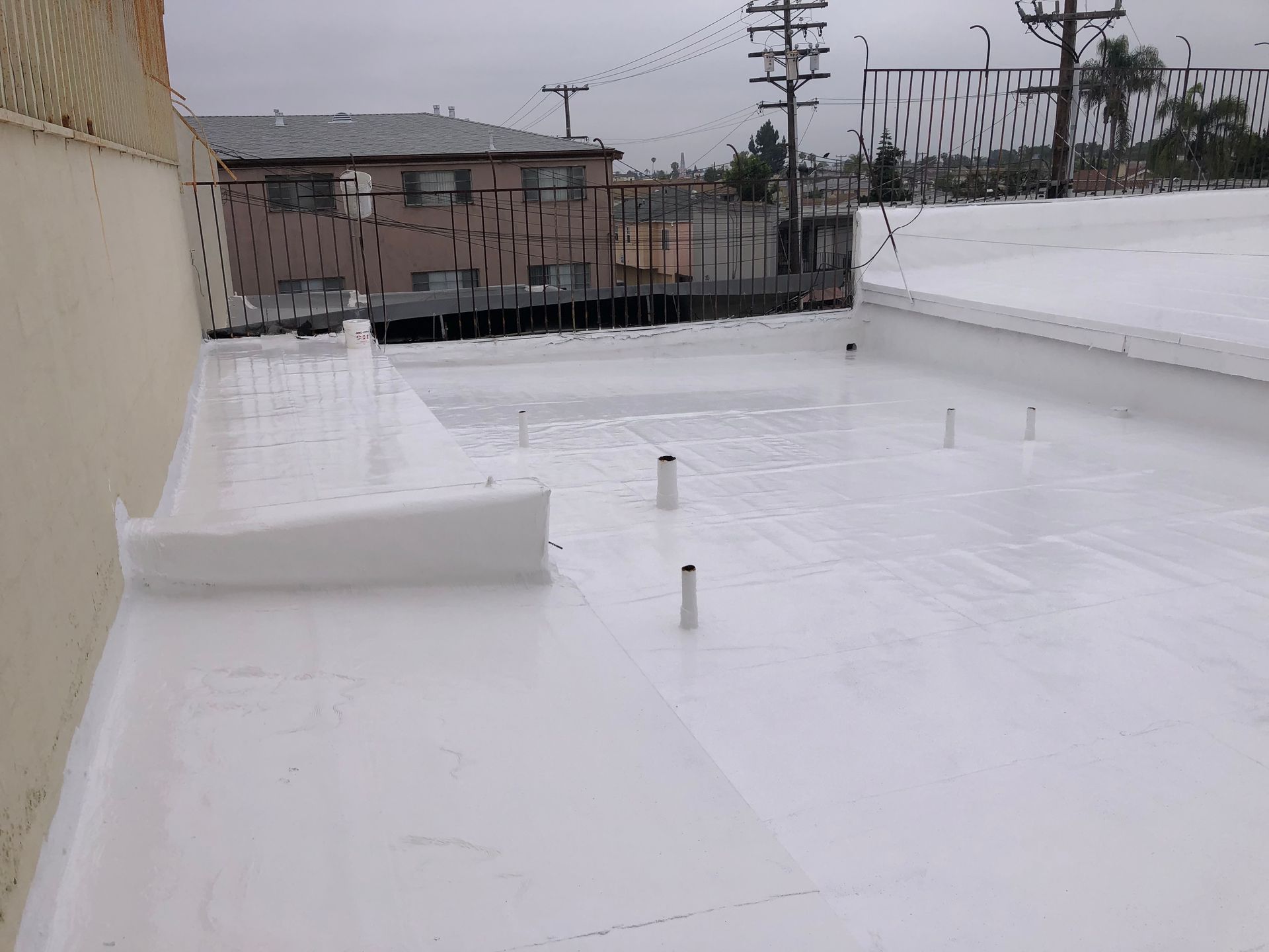 White-coated flat roof with vent pipes, overlooking buildings and a power line against a cloudy sky.