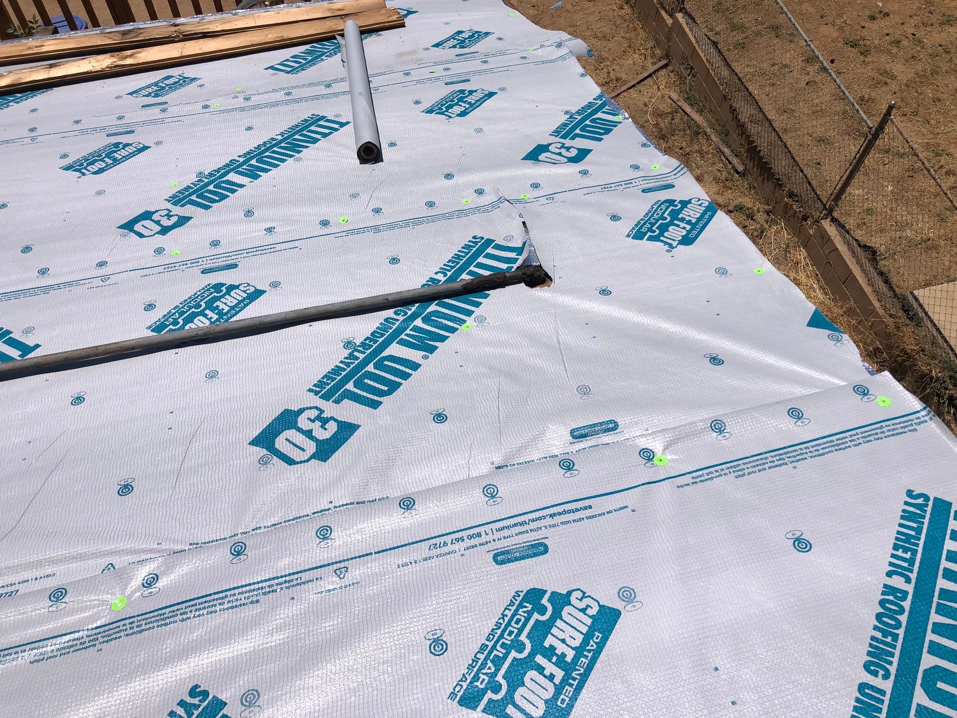White roofing underlayment with blue lettering on a roof, with a pipe running across it.