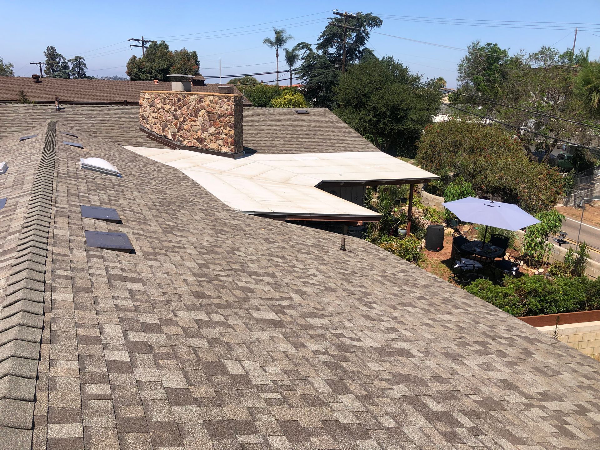 Shingled rooftops with a brick chimney, patio with umbrella, and blue sky.