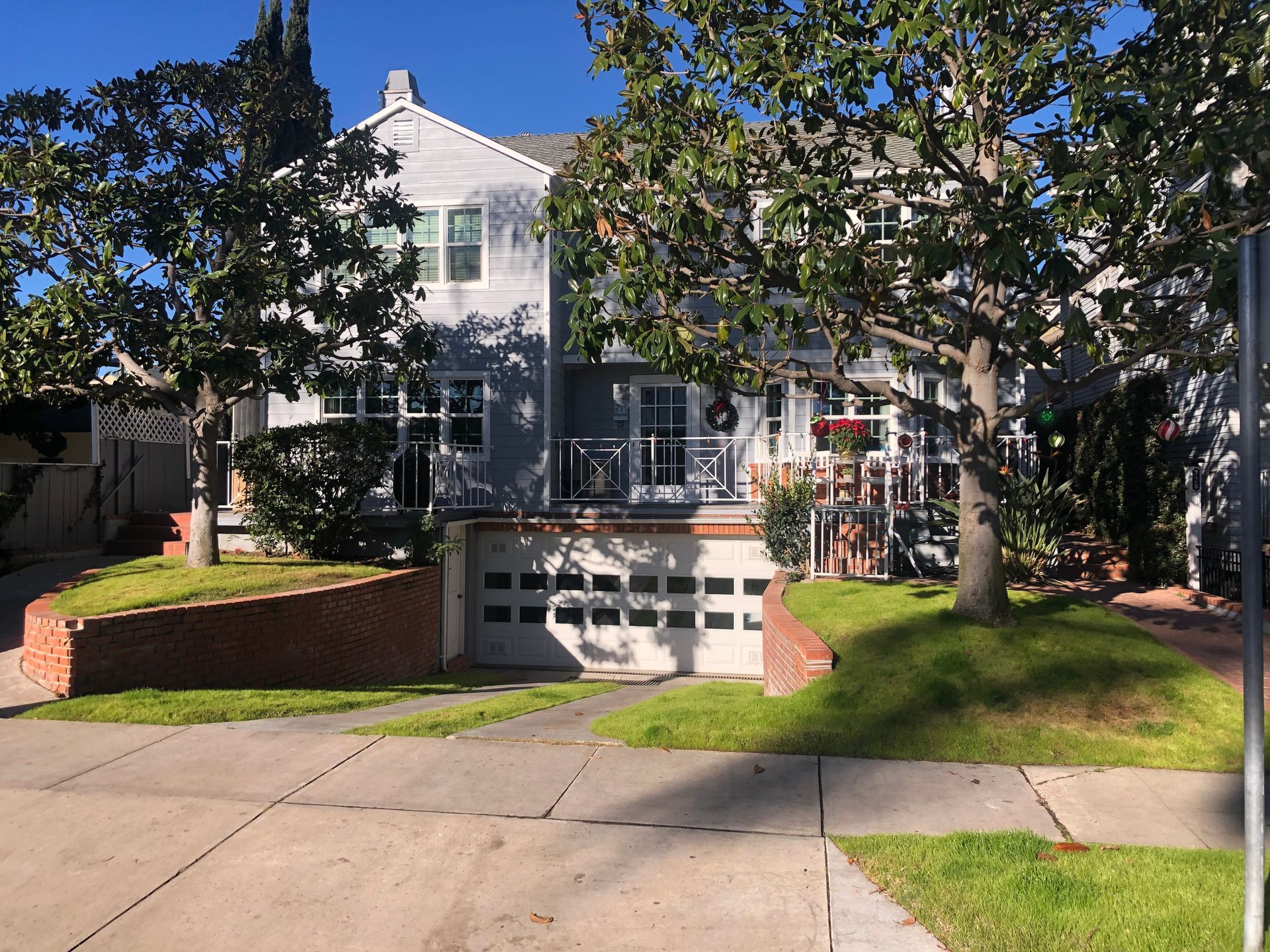 Two-story gray house with a garage, brick retaining wall, and two trees in front.