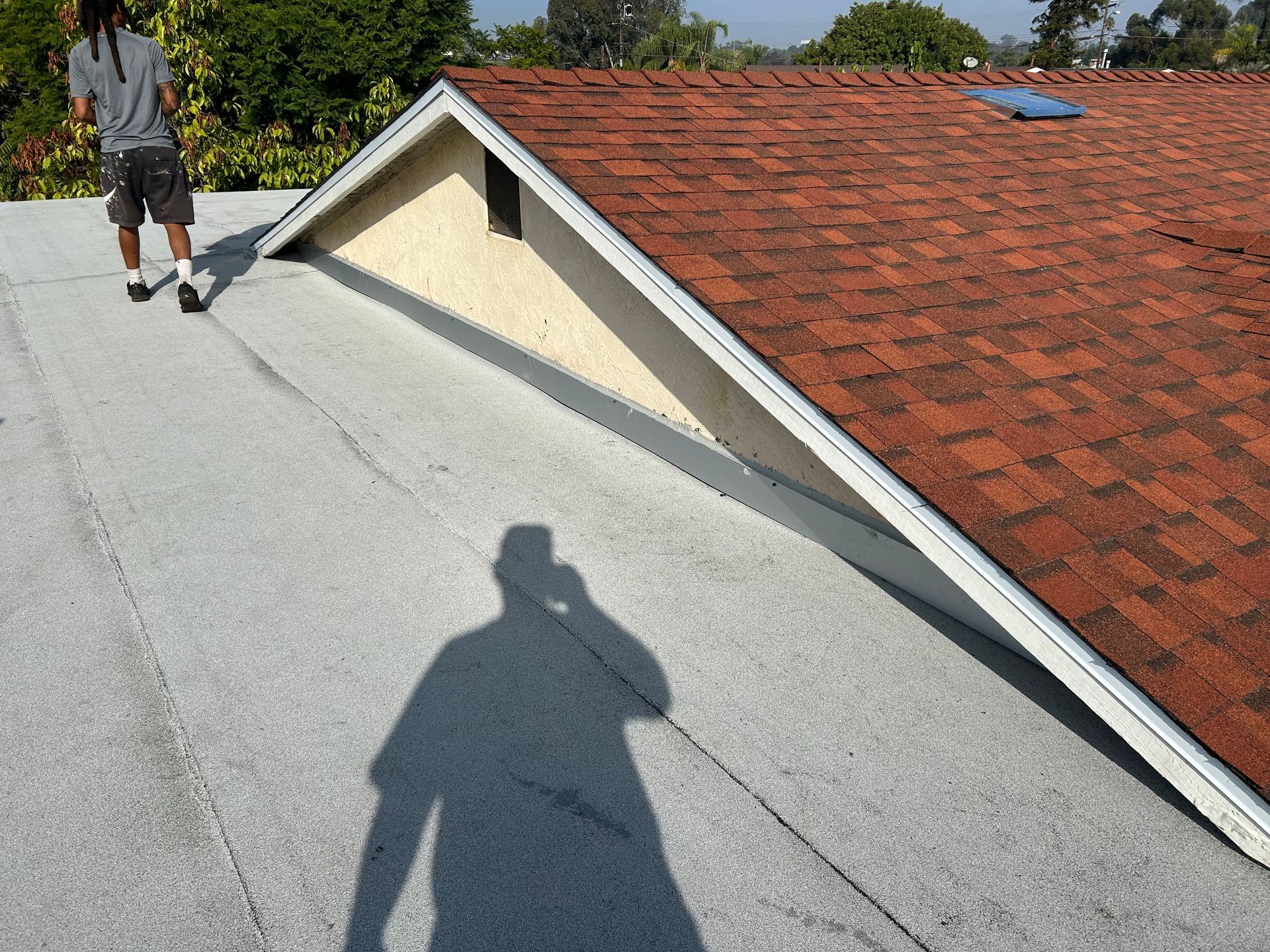 Person on a flat roof, shadow visible. A-frame with shingled roof and flat roof section.