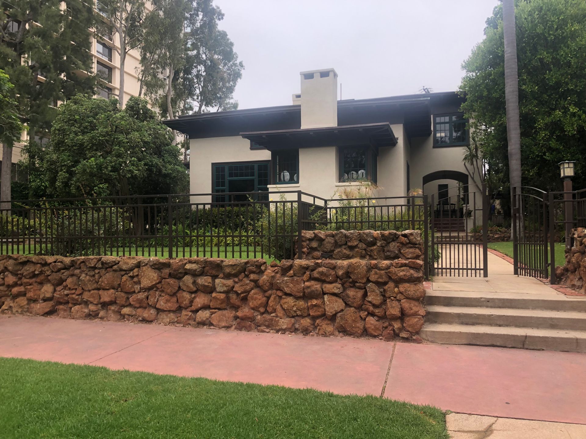 A two-story house with a stone wall, brown metal fence, and a concrete walkway.