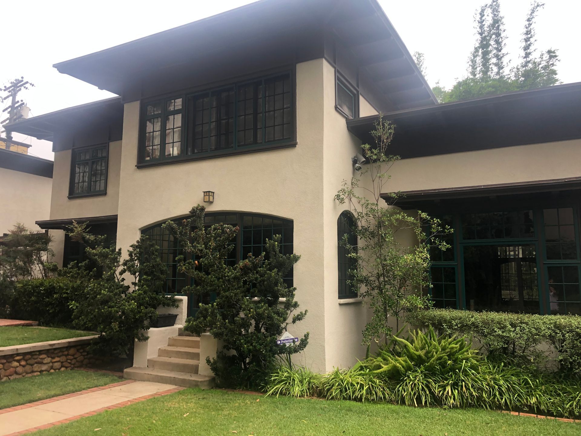 Two-story beige house with dark trim, green lawn, and landscaping; steps lead to the entrance.