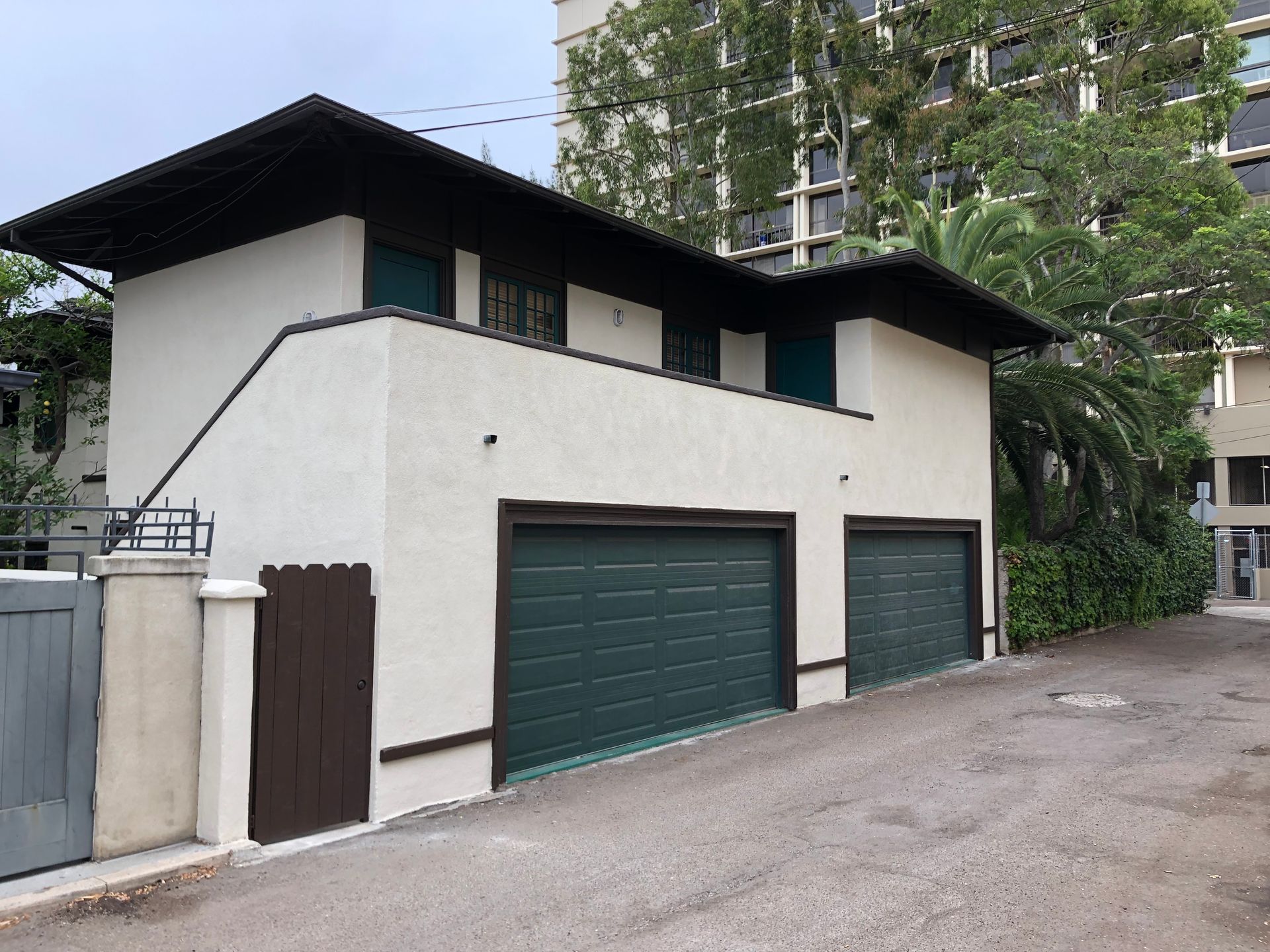 Two-story white building with green garage doors; driveway, brown trim, dark roof.