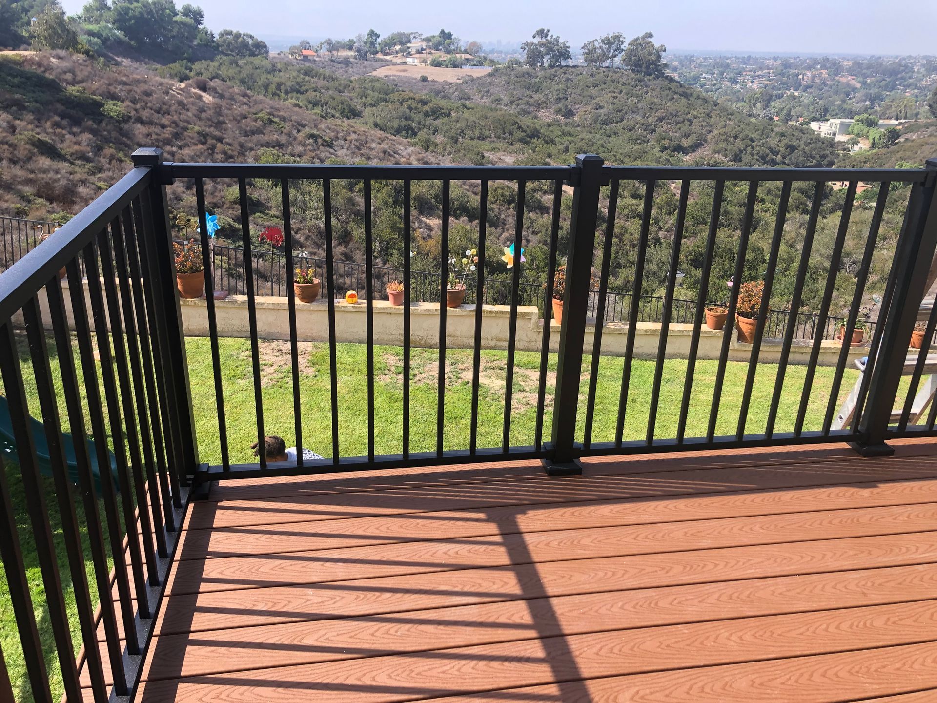 Deck with black railing overlooking a hillside with green grass and trees.