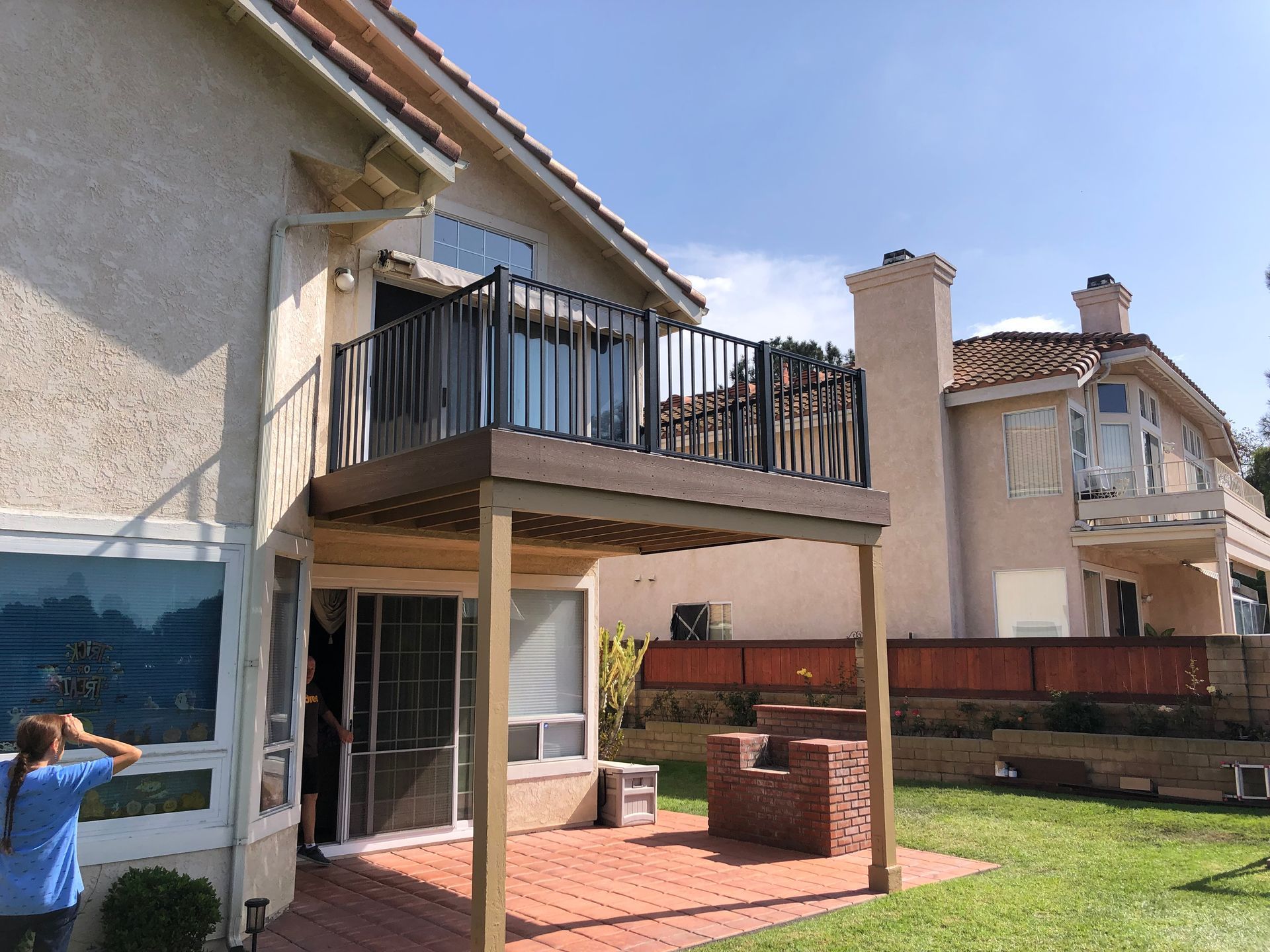 A two-story house with a deck, brick patio, and a person outside.