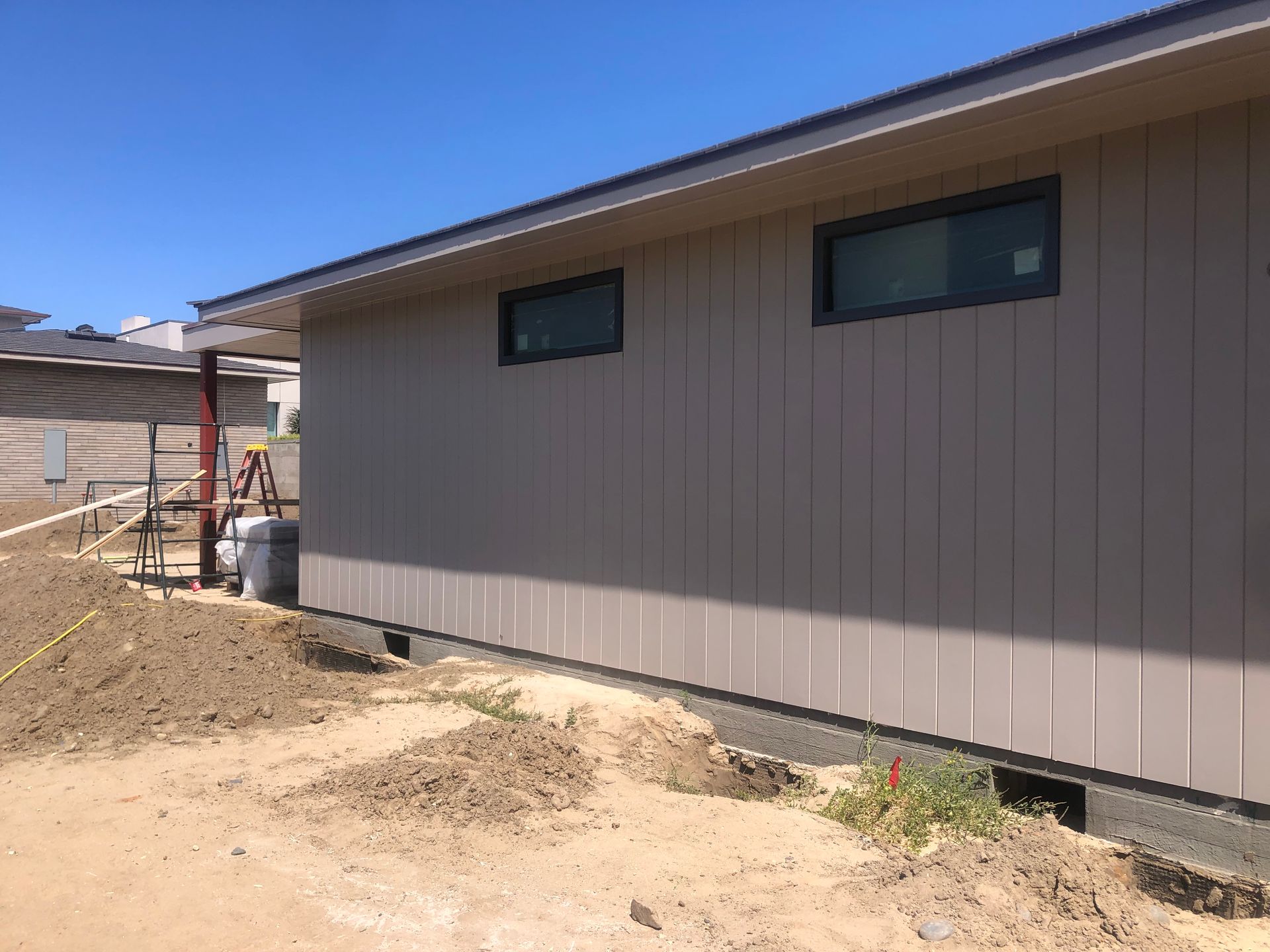 Tan building under construction with two windows, surrounded by dirt, blue sky.