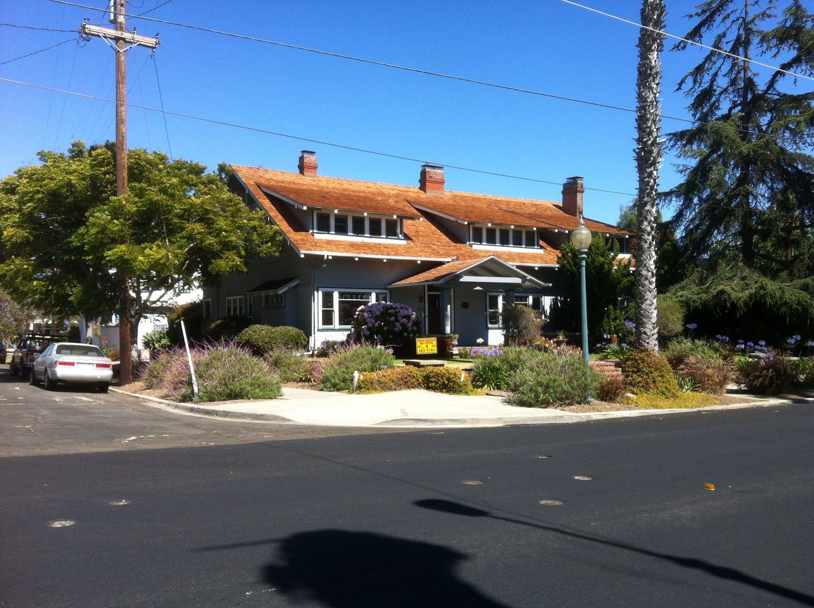 Two-story blue house with brown roof and garden, on corner lot.