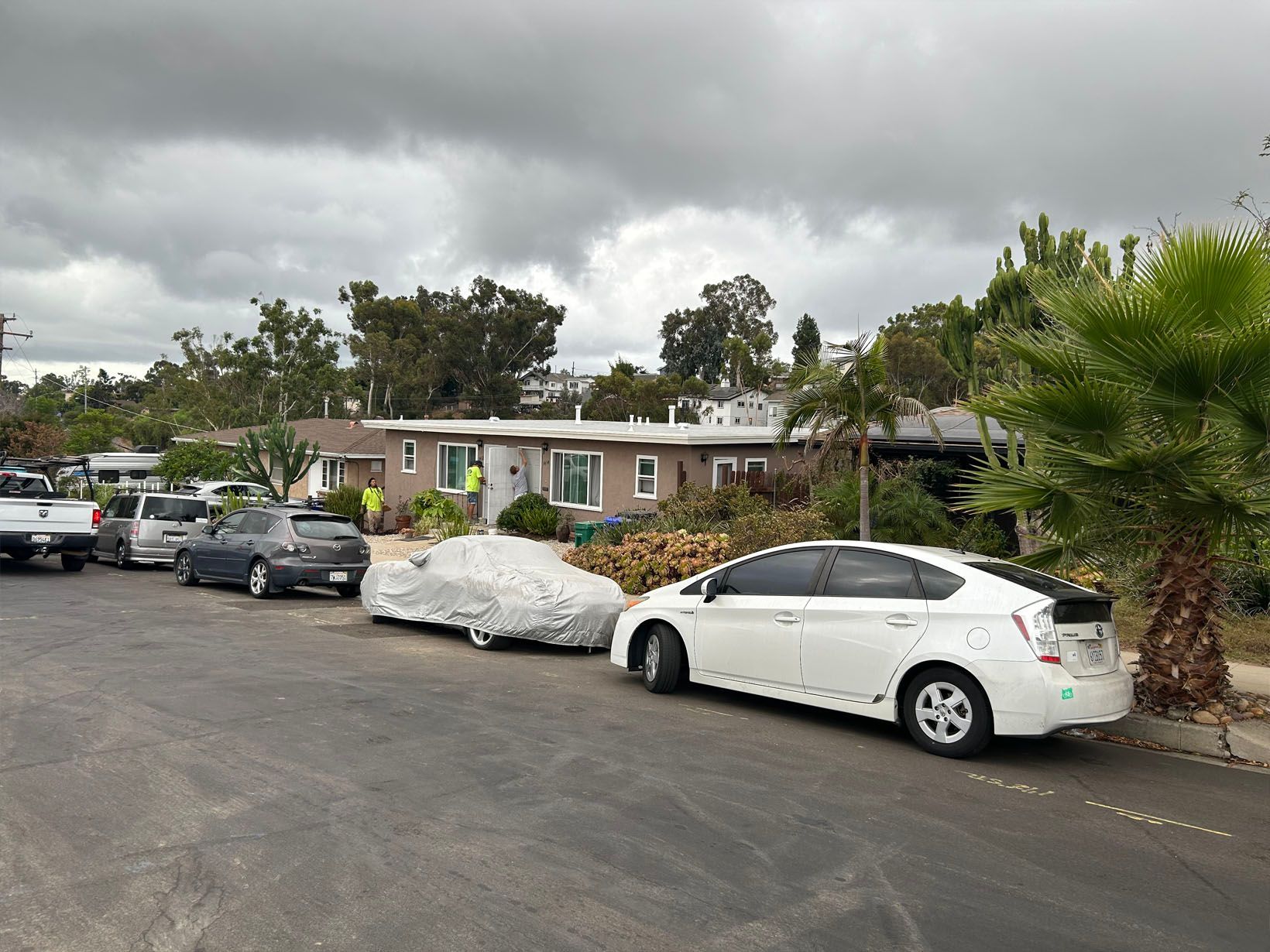 Cars parked on street in front of a house; overcast sky.