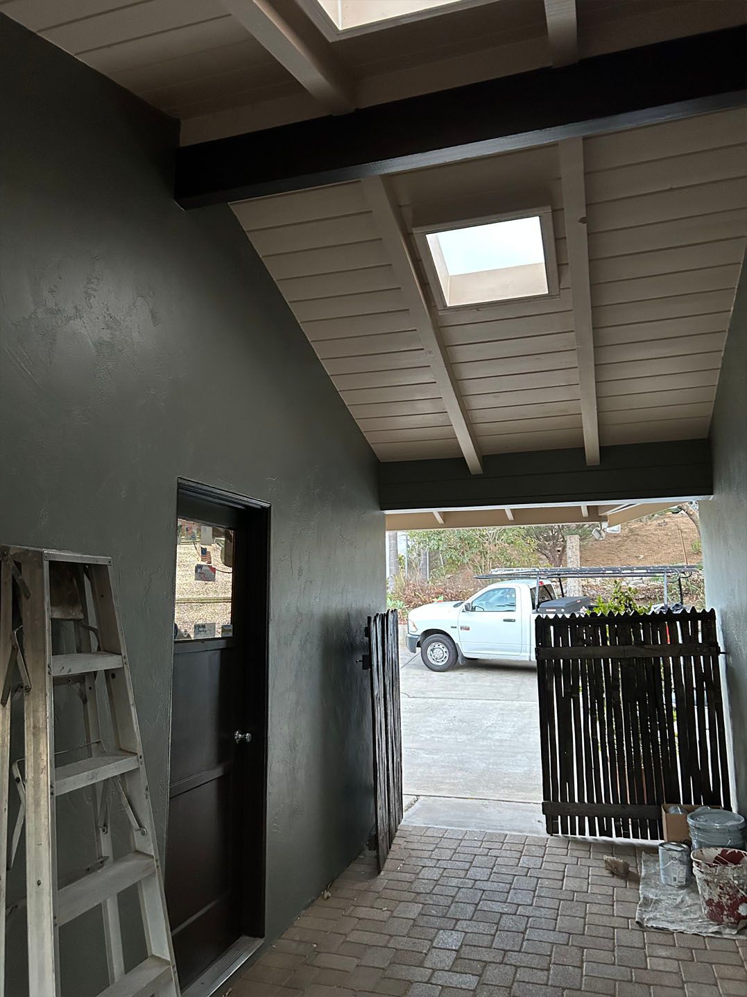 Narrow covered passageway with dark green walls, brown door, and skylights. A truck is visible at the end.