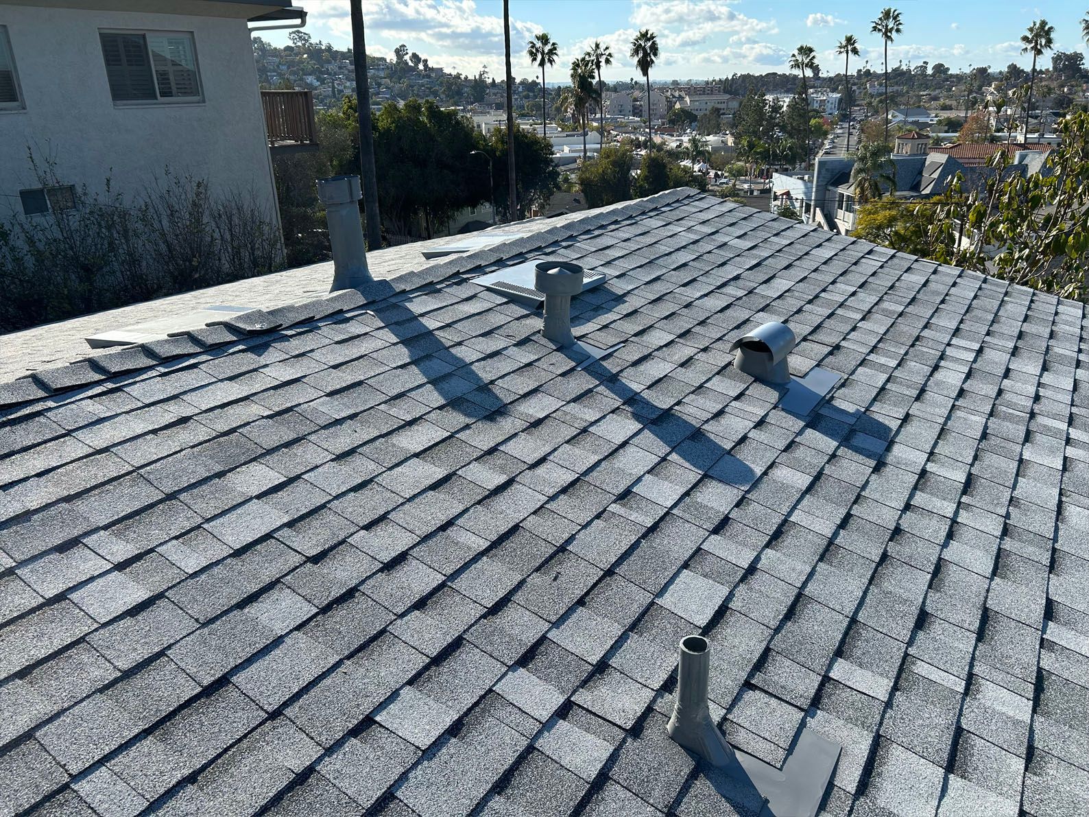 Gray shingled roof with vents, in a residential area with city views.