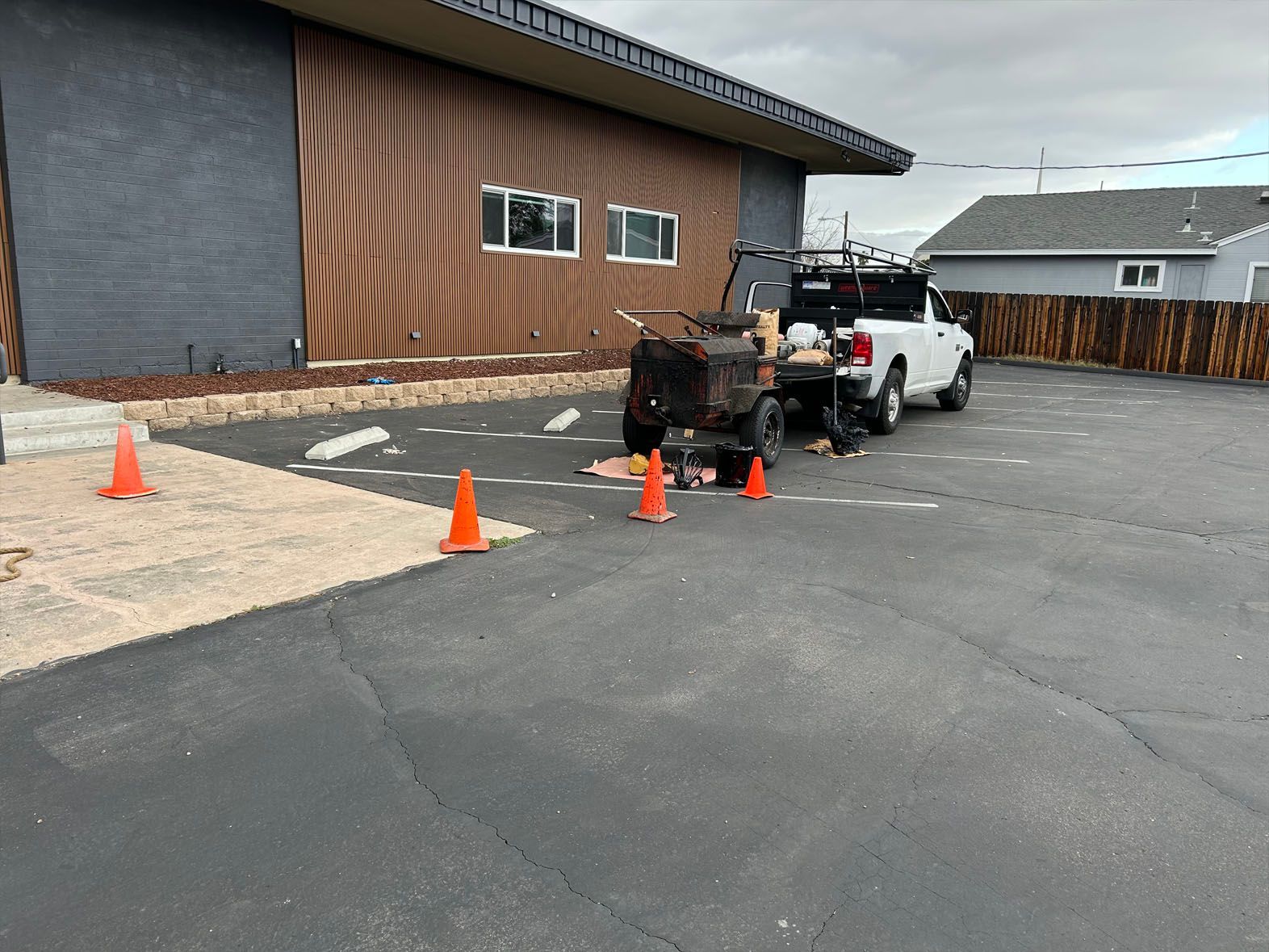 Workers seal cracks in asphalt parking lot with truck nearby, orange cones present.
