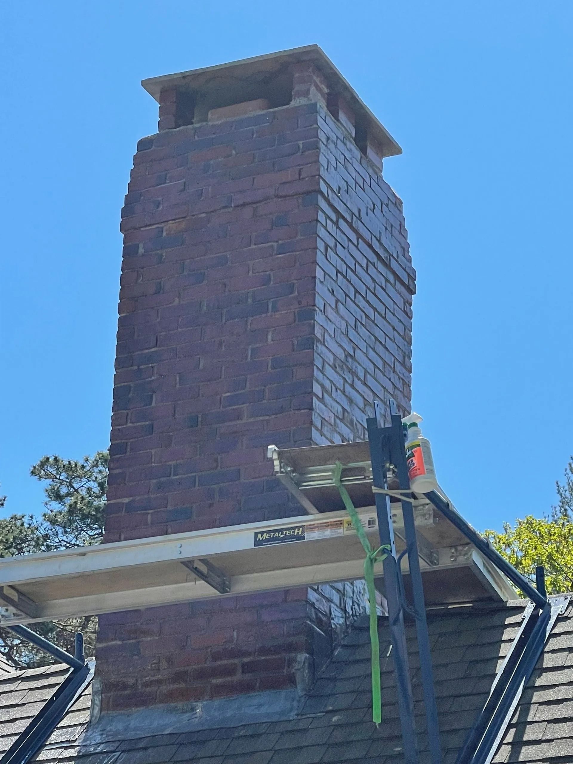 Brick chimney with scaffolding against a blue sky.