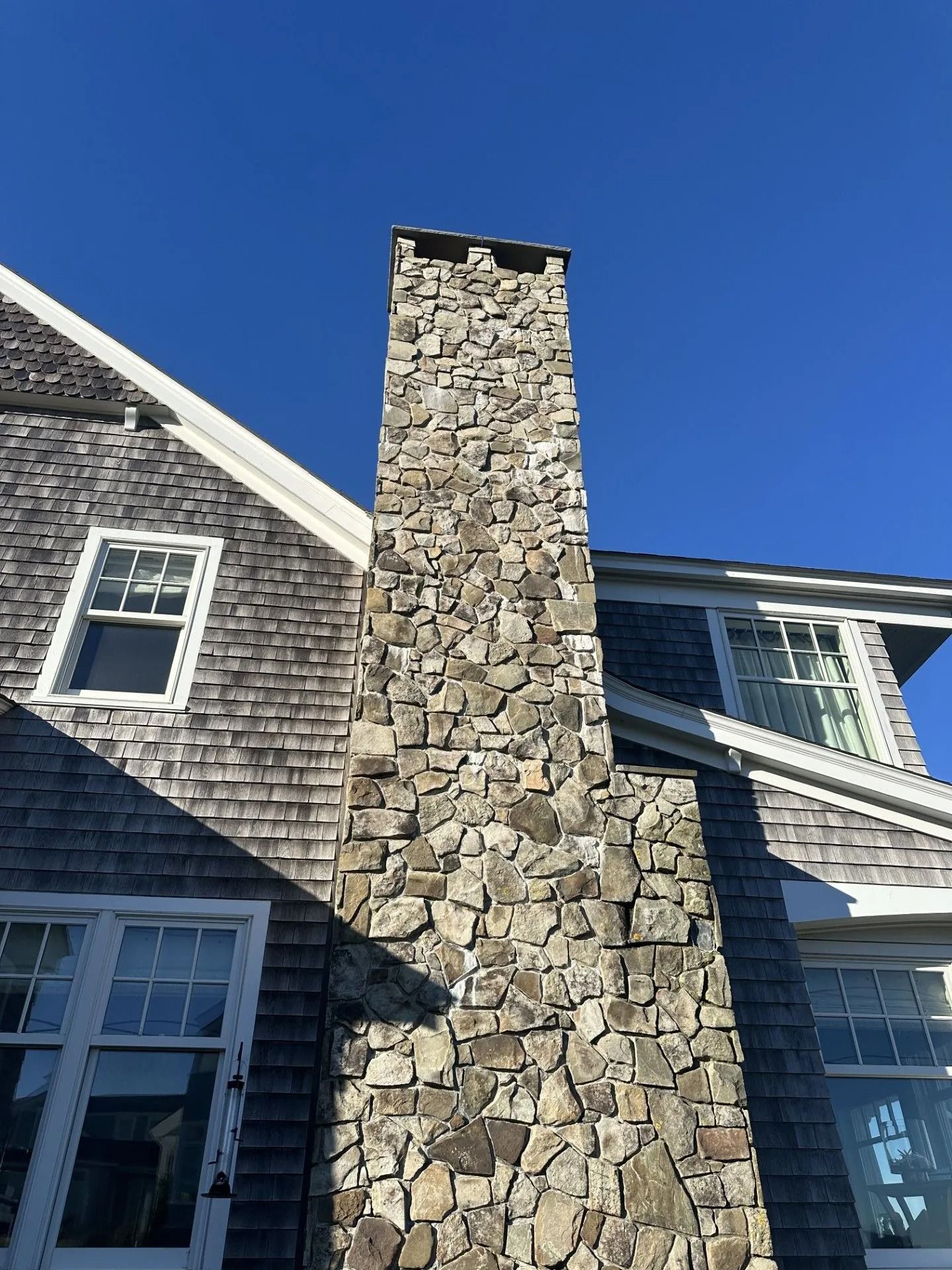 Stone chimney on a shingled building against a clear blue sky.