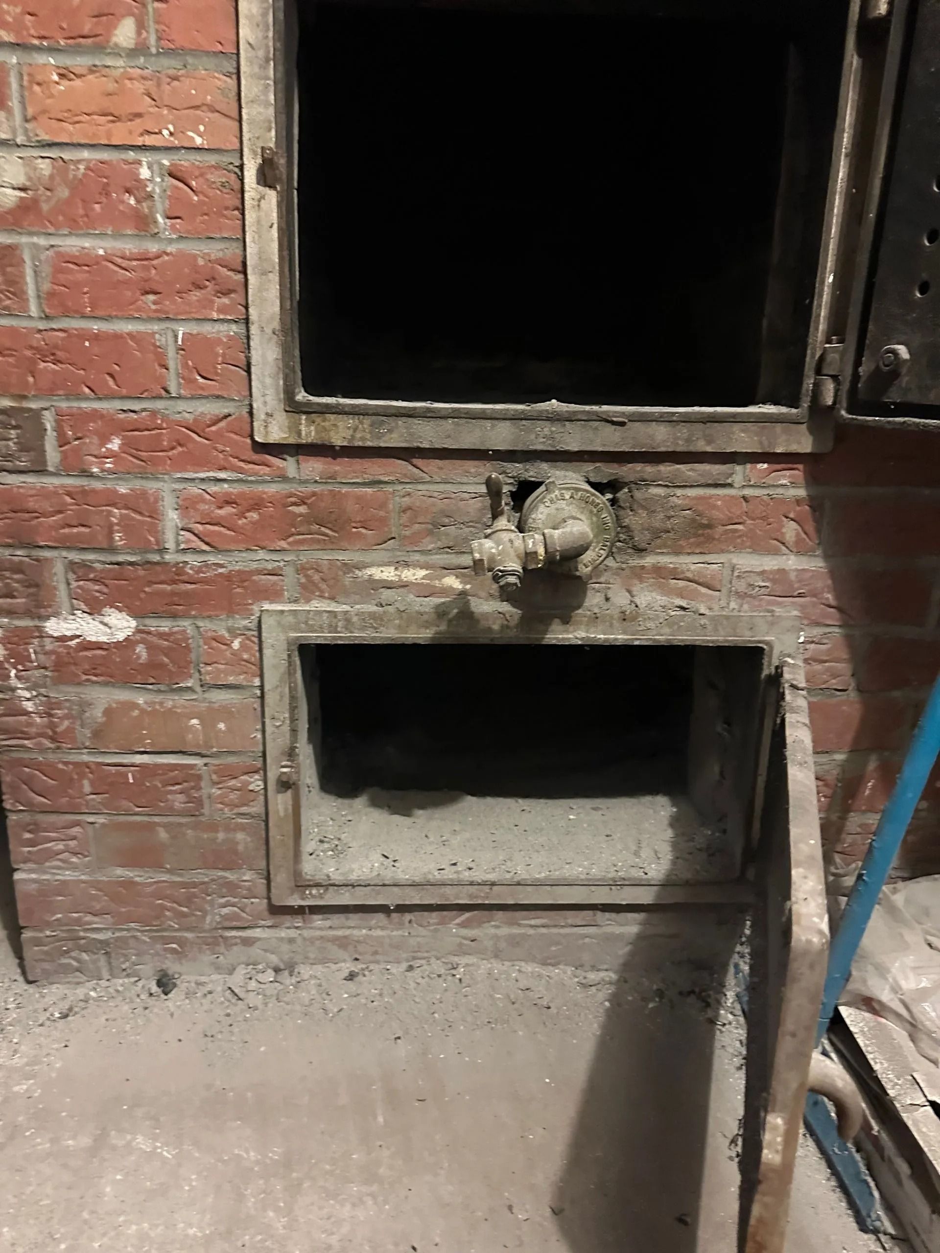 Brick furnace with open doors, showing interior ash accumulation.