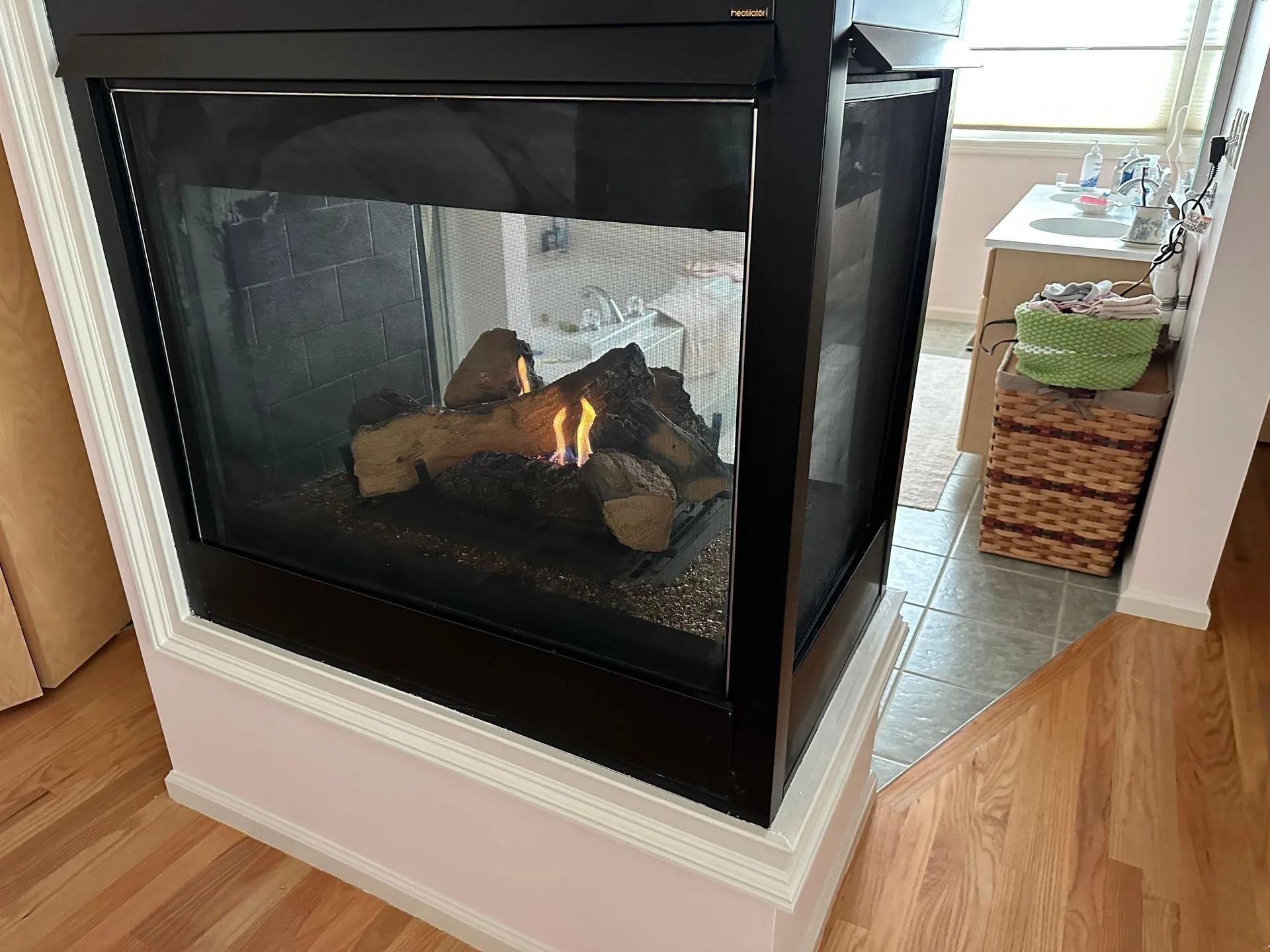 Fireplace with a black frame and decorative logs, set in a light-colored corner wall.