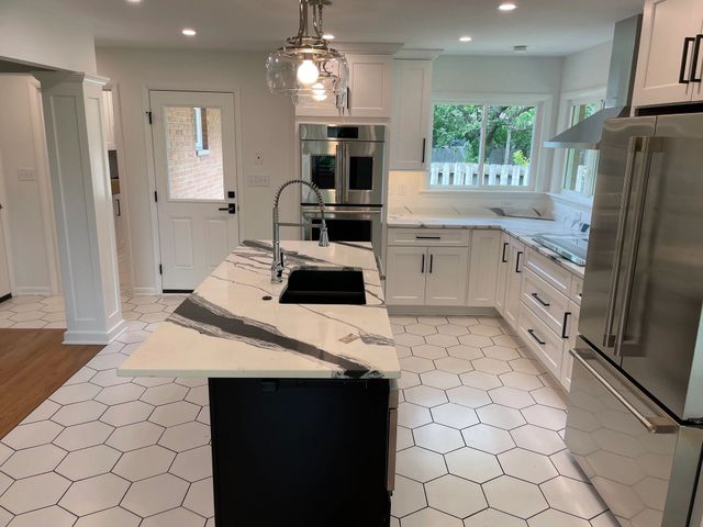 Modern white kitchen with black island, stainless steel appliances, and geometric floor tiles.