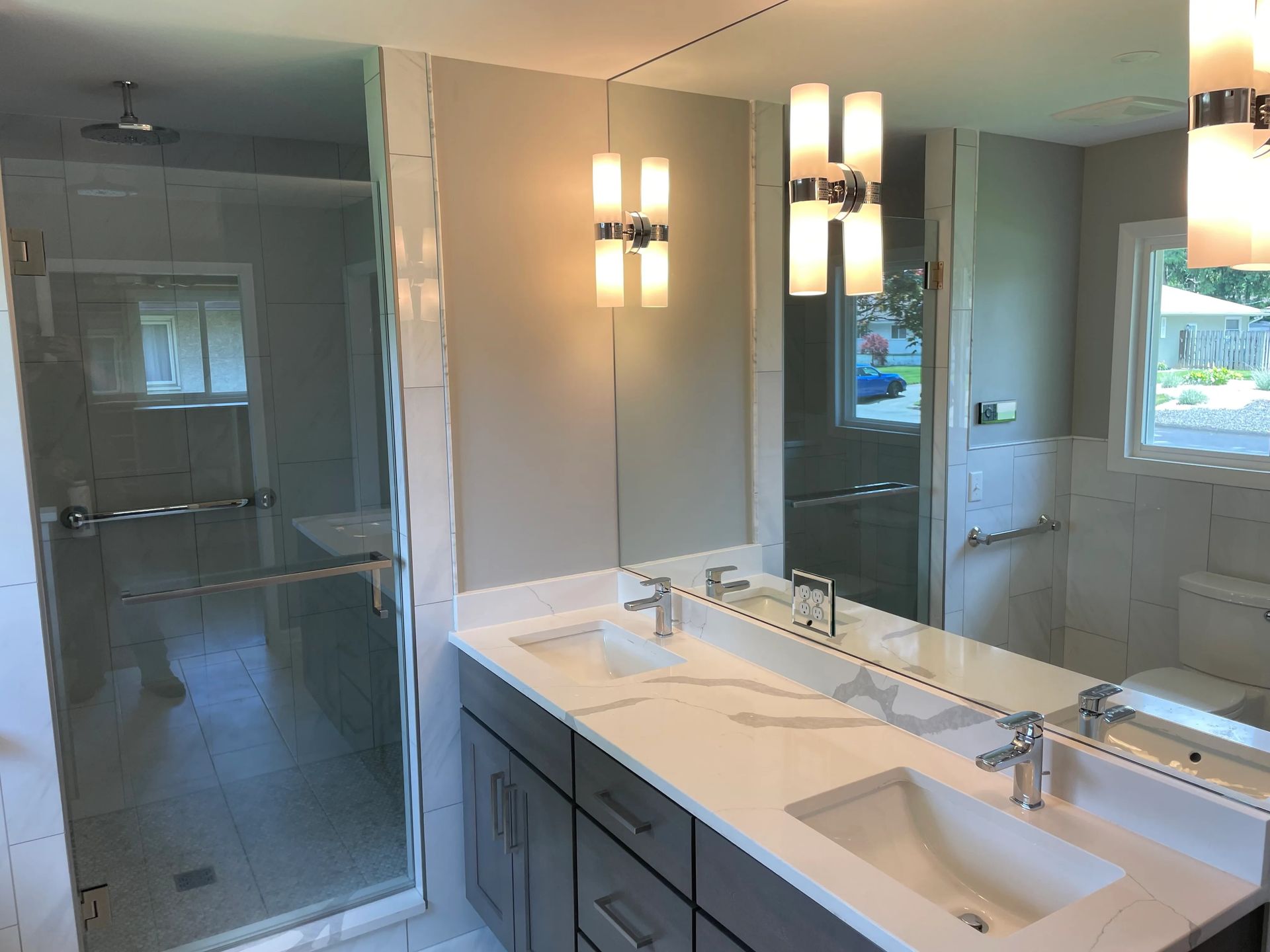Modern bathroom with a glass shower, double sinks, and bright wall sconces.
