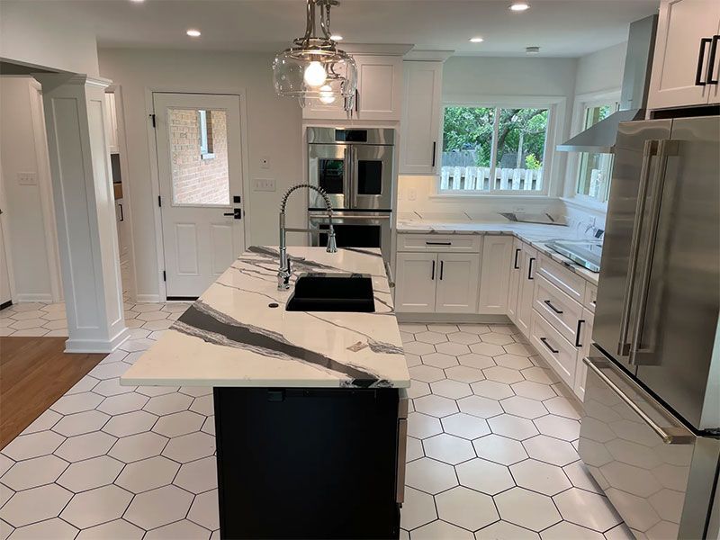 Modern white kitchen with a black island, white countertops, and hexagon tile floor.