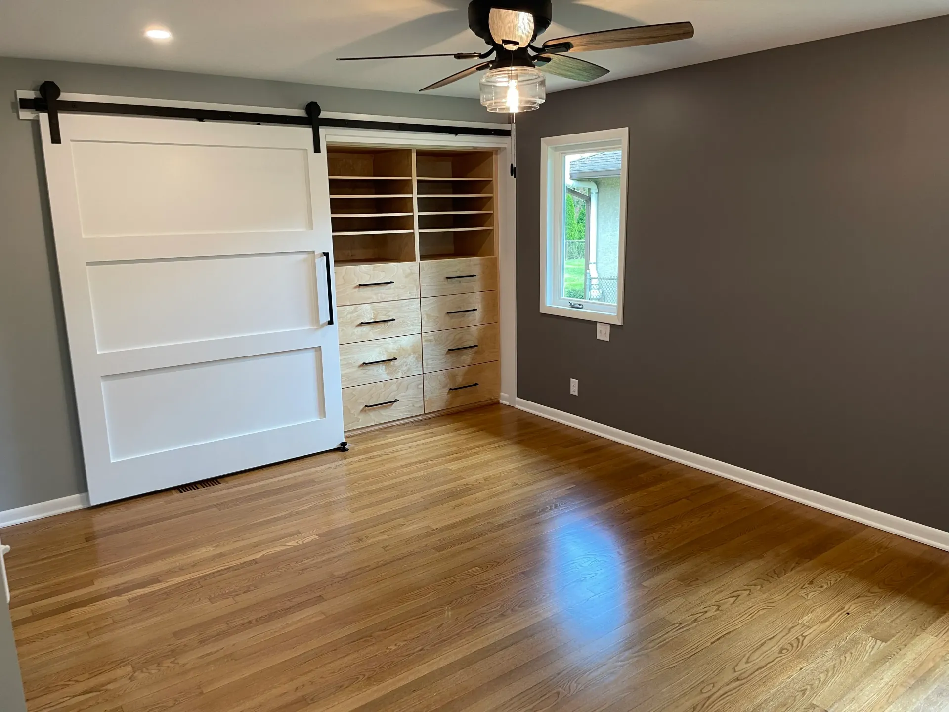 Bedroom with wood floors, barn door closet, and gray walls; natural light from small window.